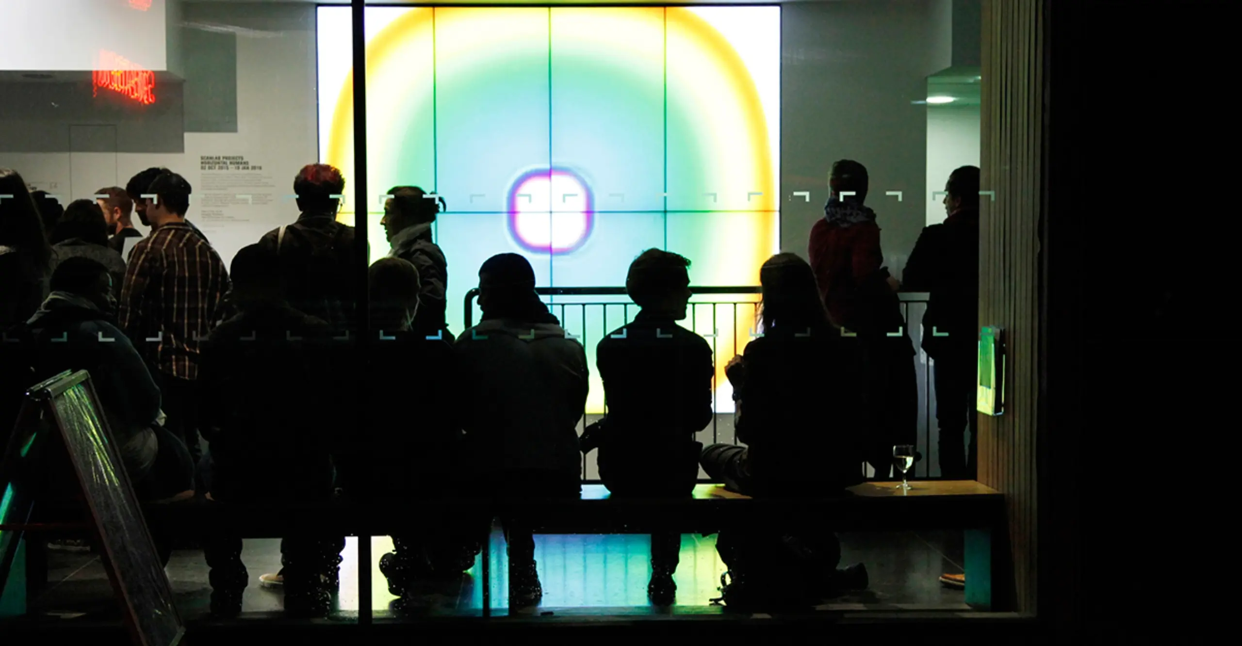 A group of people sitting on a bench against a big screen showing a yellow and green circle