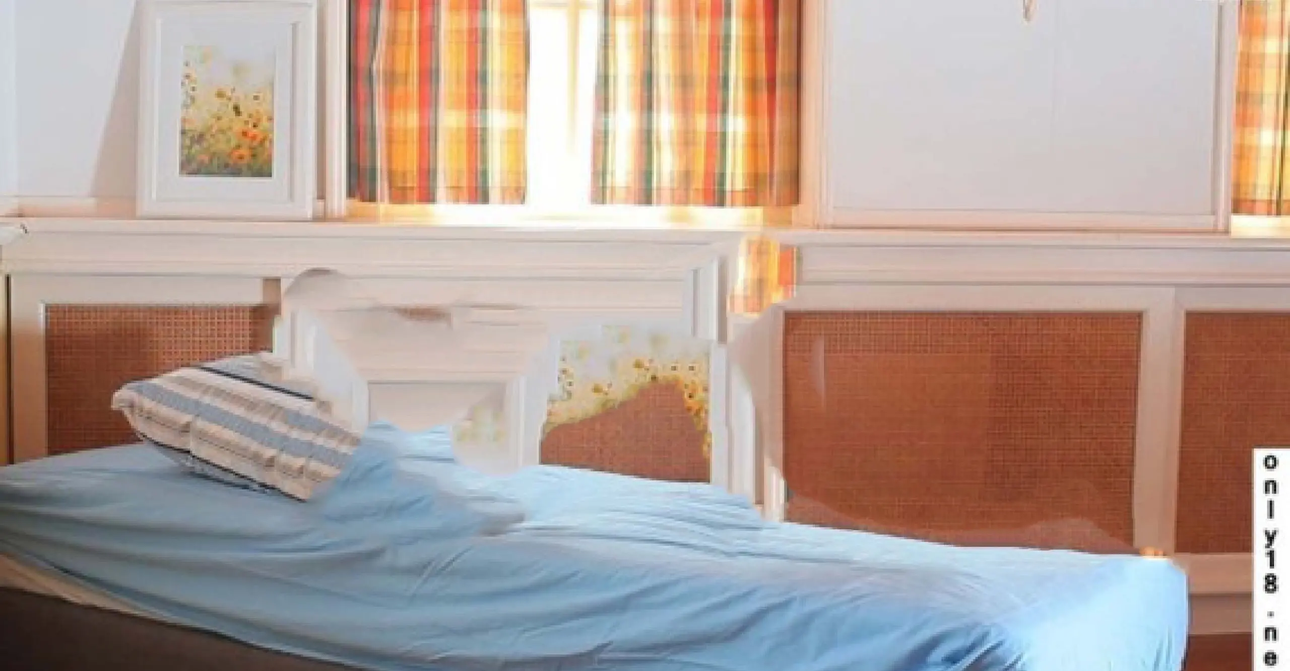 An image of a room with white walls, orange curtains, a bed with blue sheets and a person digitally removed 