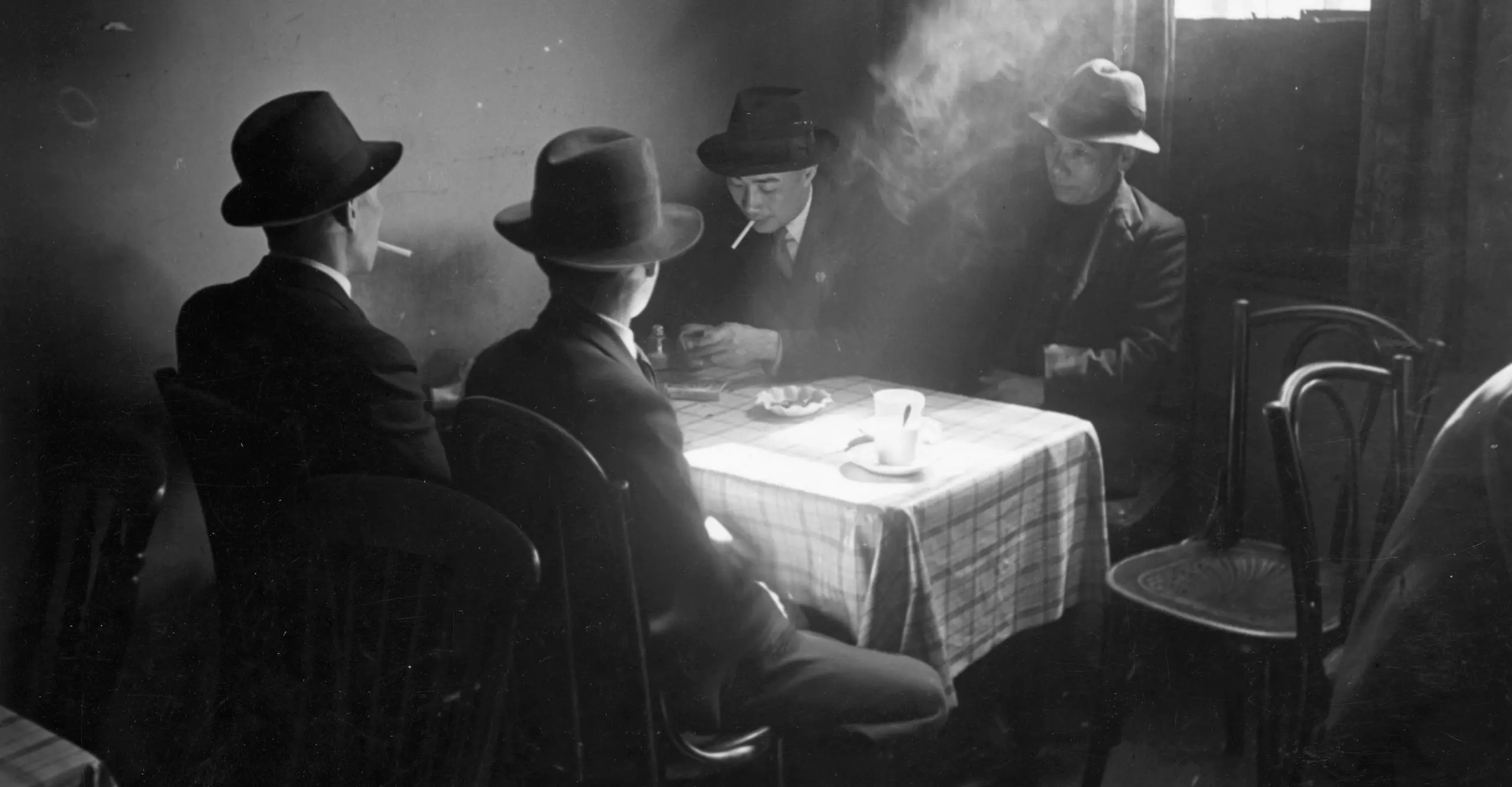 Black and white photo of a group of men sitting around a table in a Chinese hostel in Liverpool.