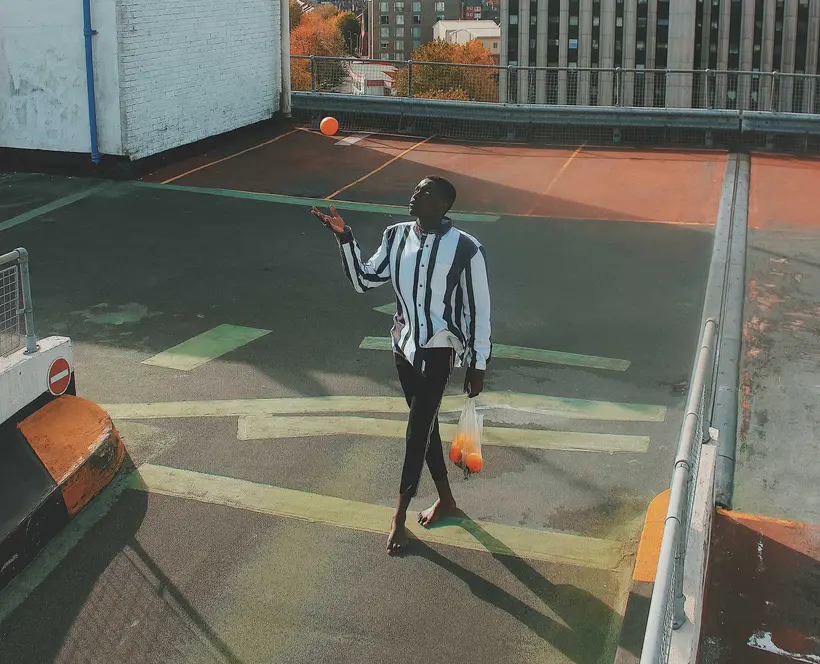 A man walking across a parking lot throwing an orange