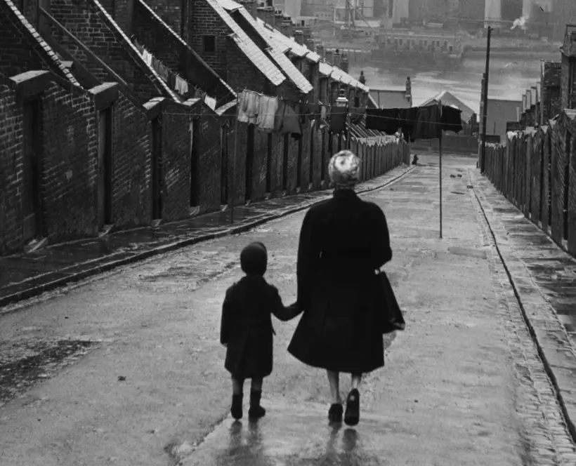 Black and white photo of a woman and child walking down a residential street.