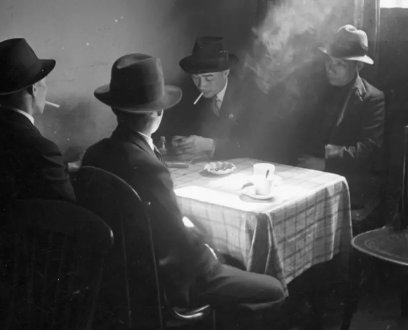 Black and white photo of a group of men sitting around a table in a Chinese hostel in Liverpool.