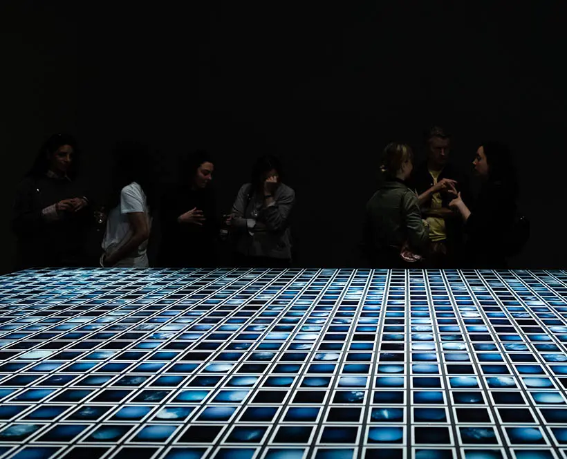 A surface covered in hundreds of polaroid photos of skies appears to stretch out to a horizon and a black backdrop