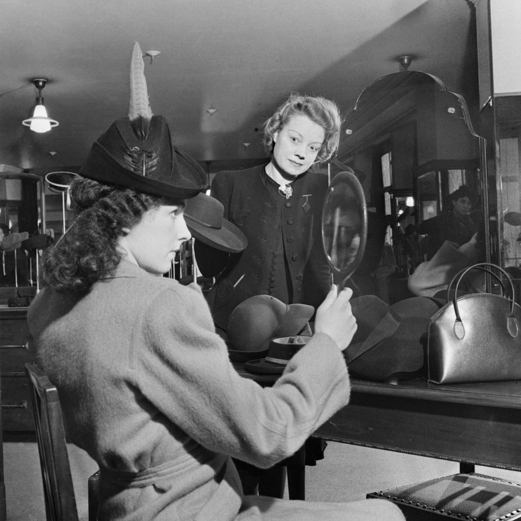 A customer tries on a new hat in the millinery department of Bourne and Hollingsworth on London's Oxford Street in 1942, released by the Imperial War Museum on the IWM Non Commercial Licence
