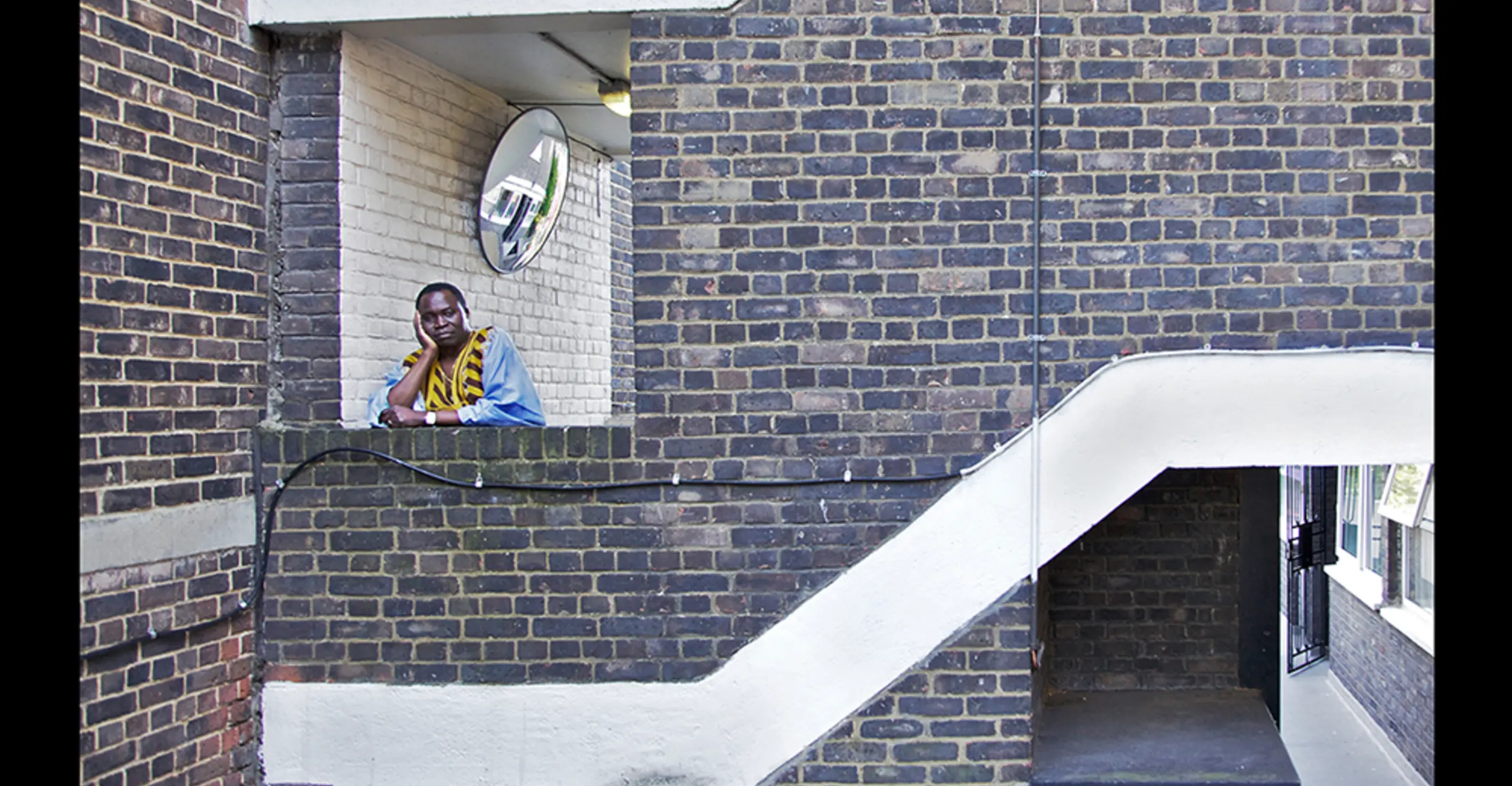 Souleymani Koanda looking at the camera on an outdoors stairway. The photographs is signed by Briony Campbell 