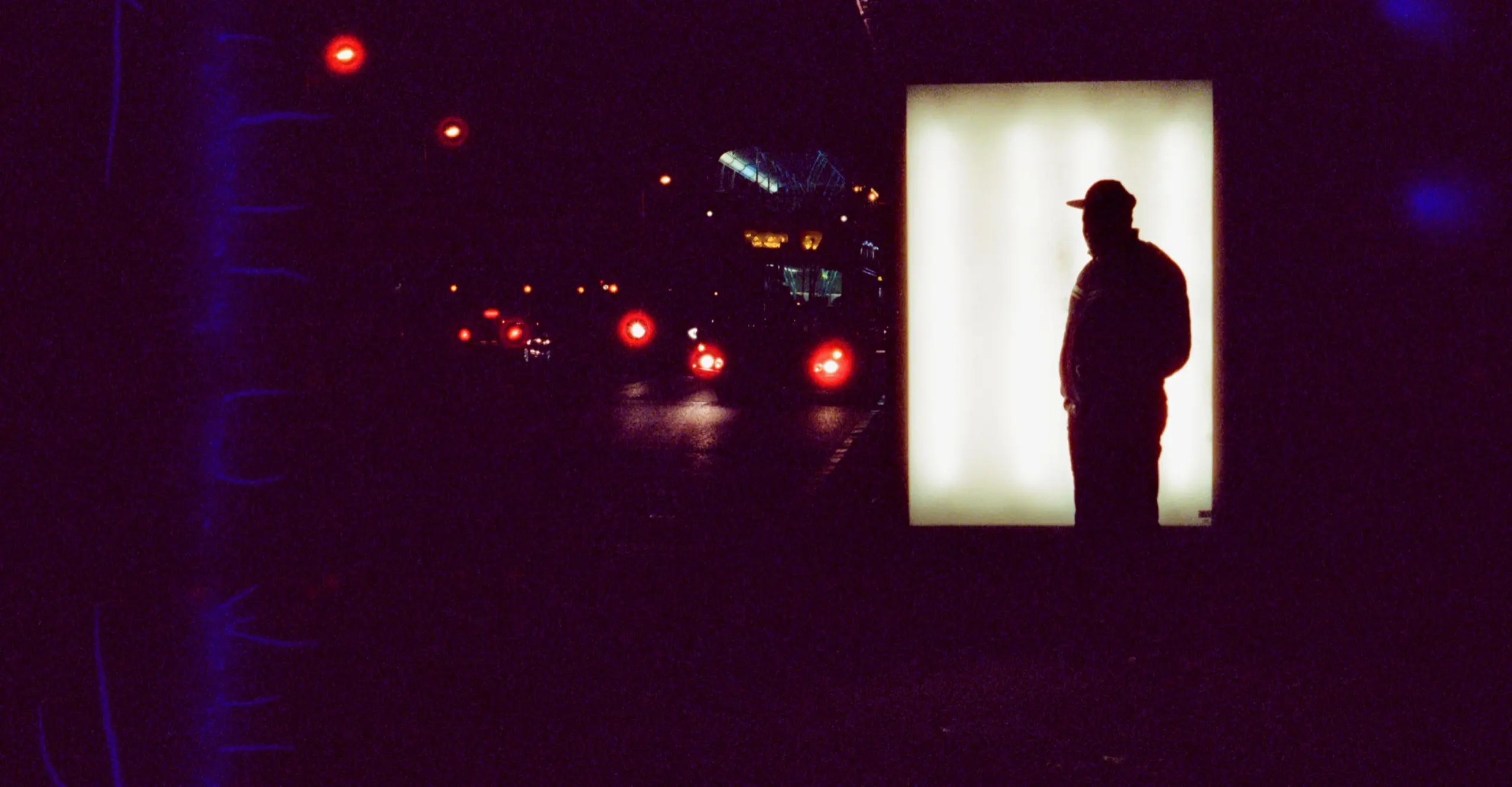 Silhouetted figure standing in front of a bus stop poster at night