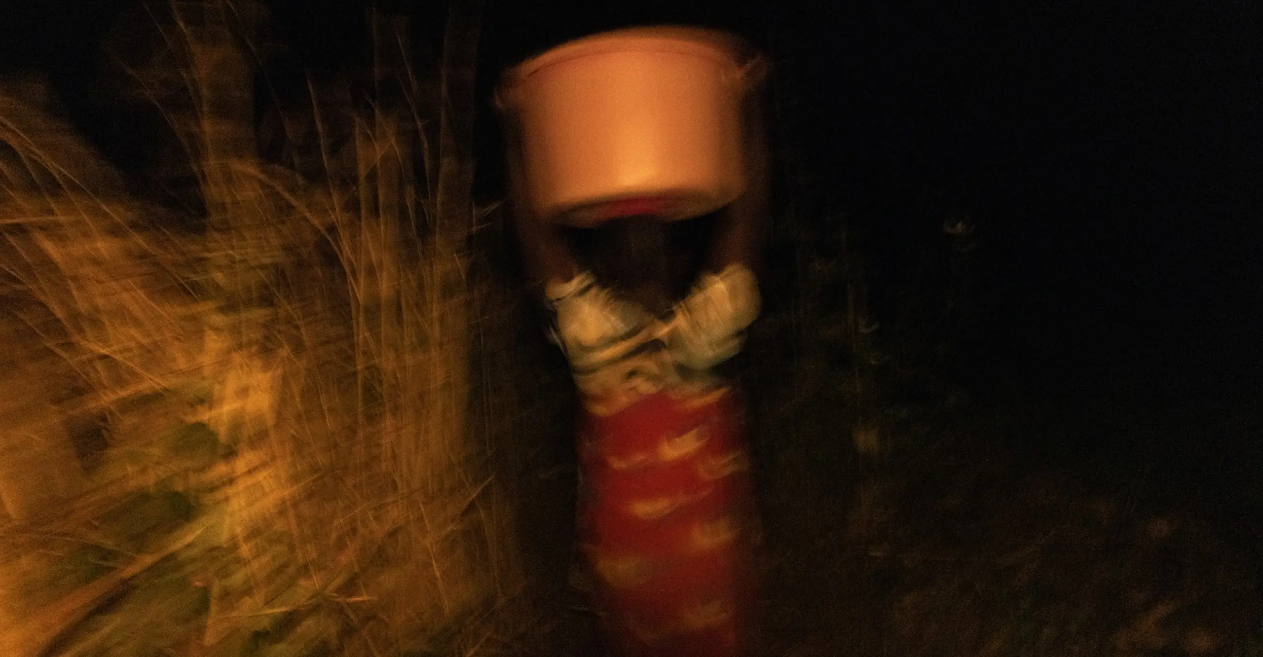 Blurred image of a person carrying a large orange bucket on their head in the darkness