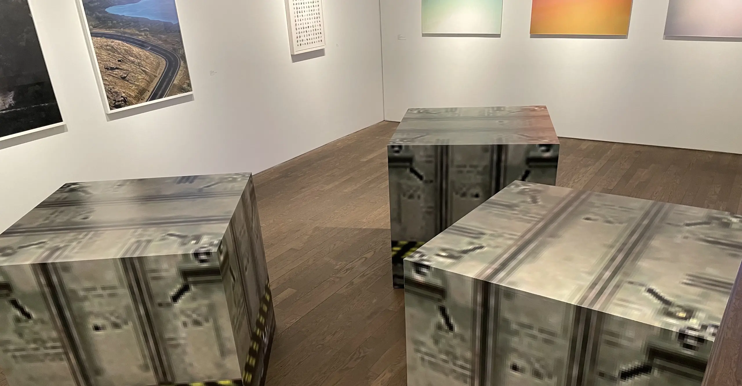 A gallery space with three sculptural cubes in the foreground that look like computer game blocks have landed into the 'real world'.