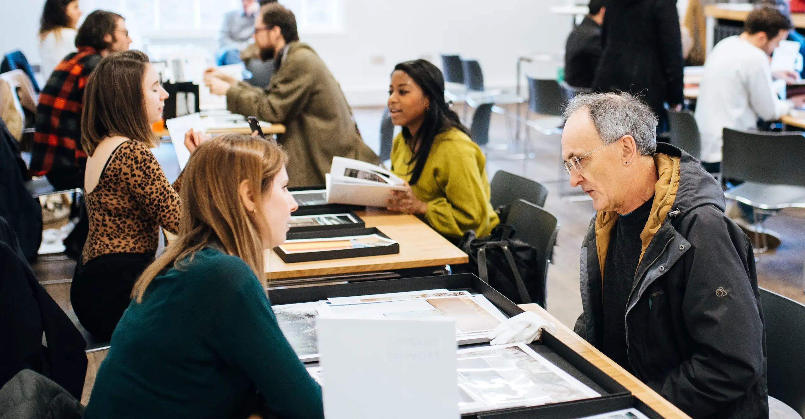Photograph of two people sitting across from each other at a table with photographs on it