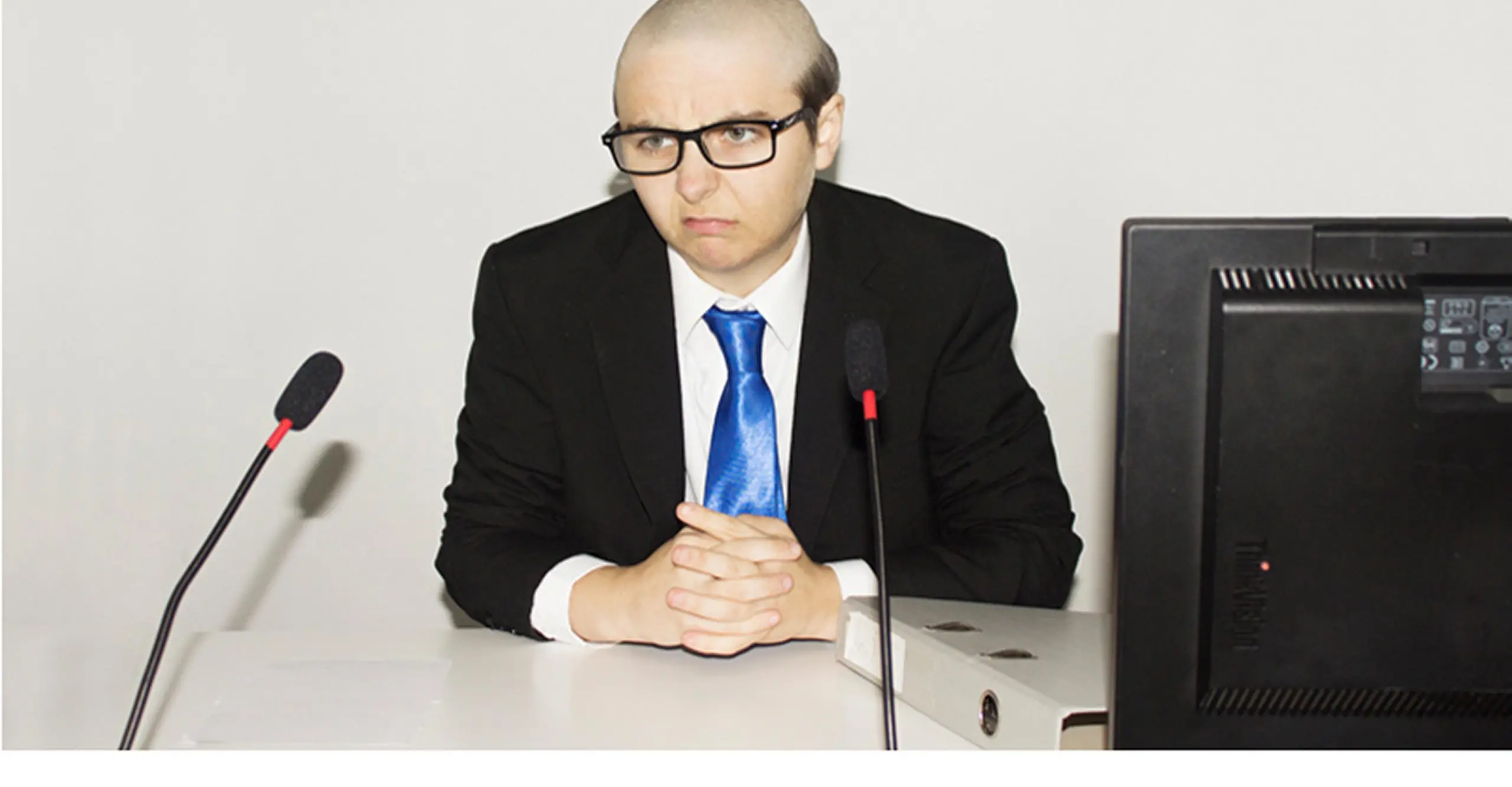 A person with no hair sat at a desk wearing a suit.