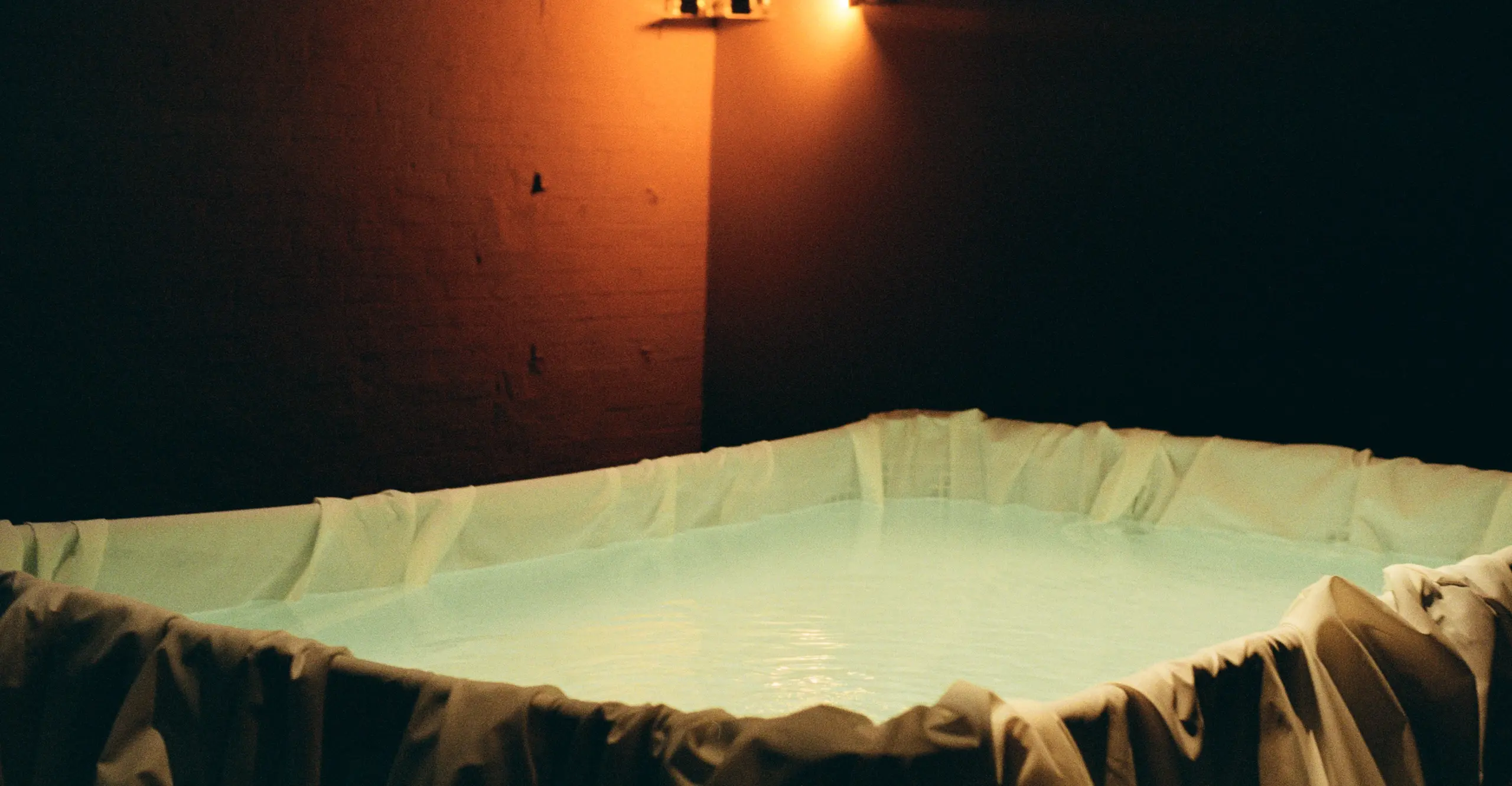 A pool is in the centre of the frame in a dimly lit room. 