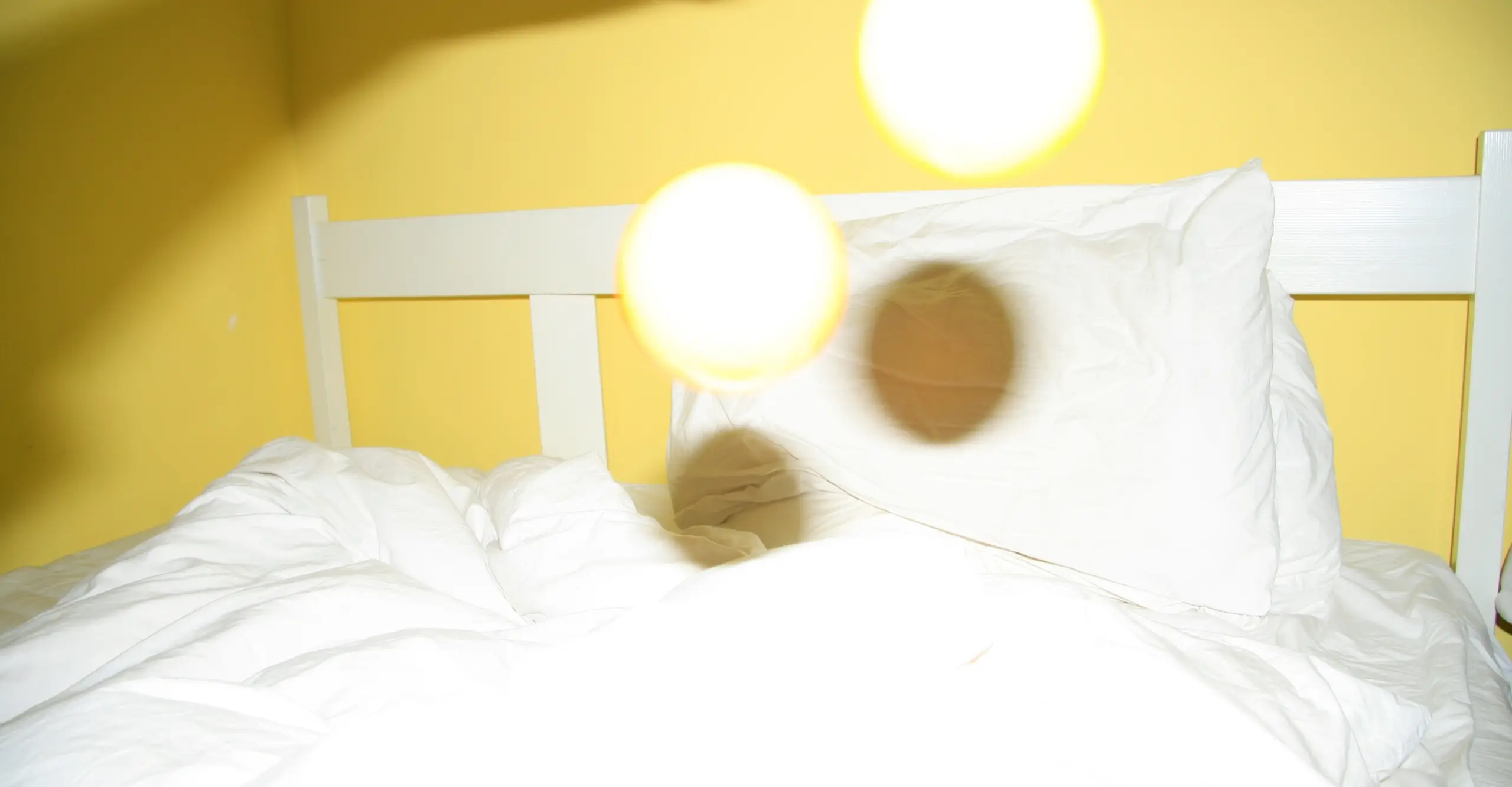 Colour interior shot featuring a white bed in a yellow room with two yellow white circles in the middle