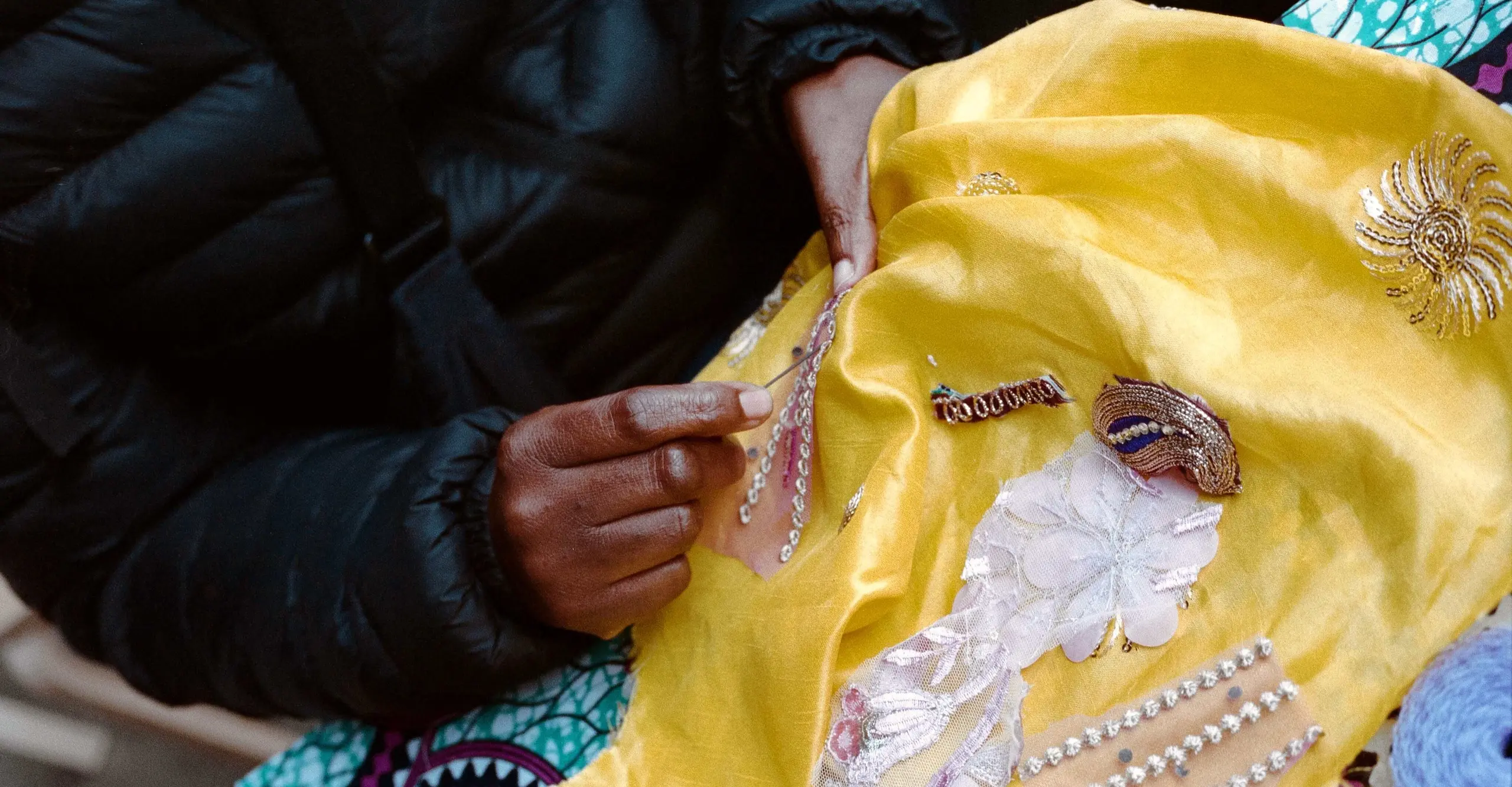 A close up of a pair of hands sewing a yellow satin cloth.