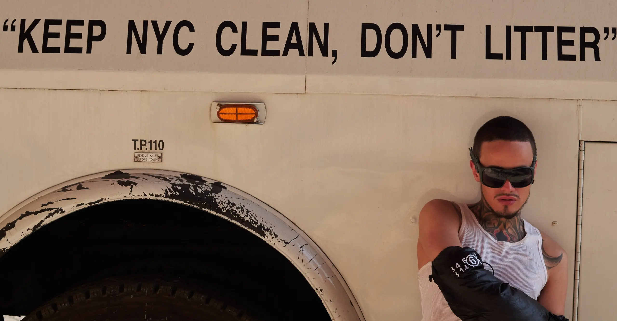 Colour photograph of a person sitting against the side of a vehicle with the words 'Keep NYC Clean, Don't Litter' on the side of the vehicle