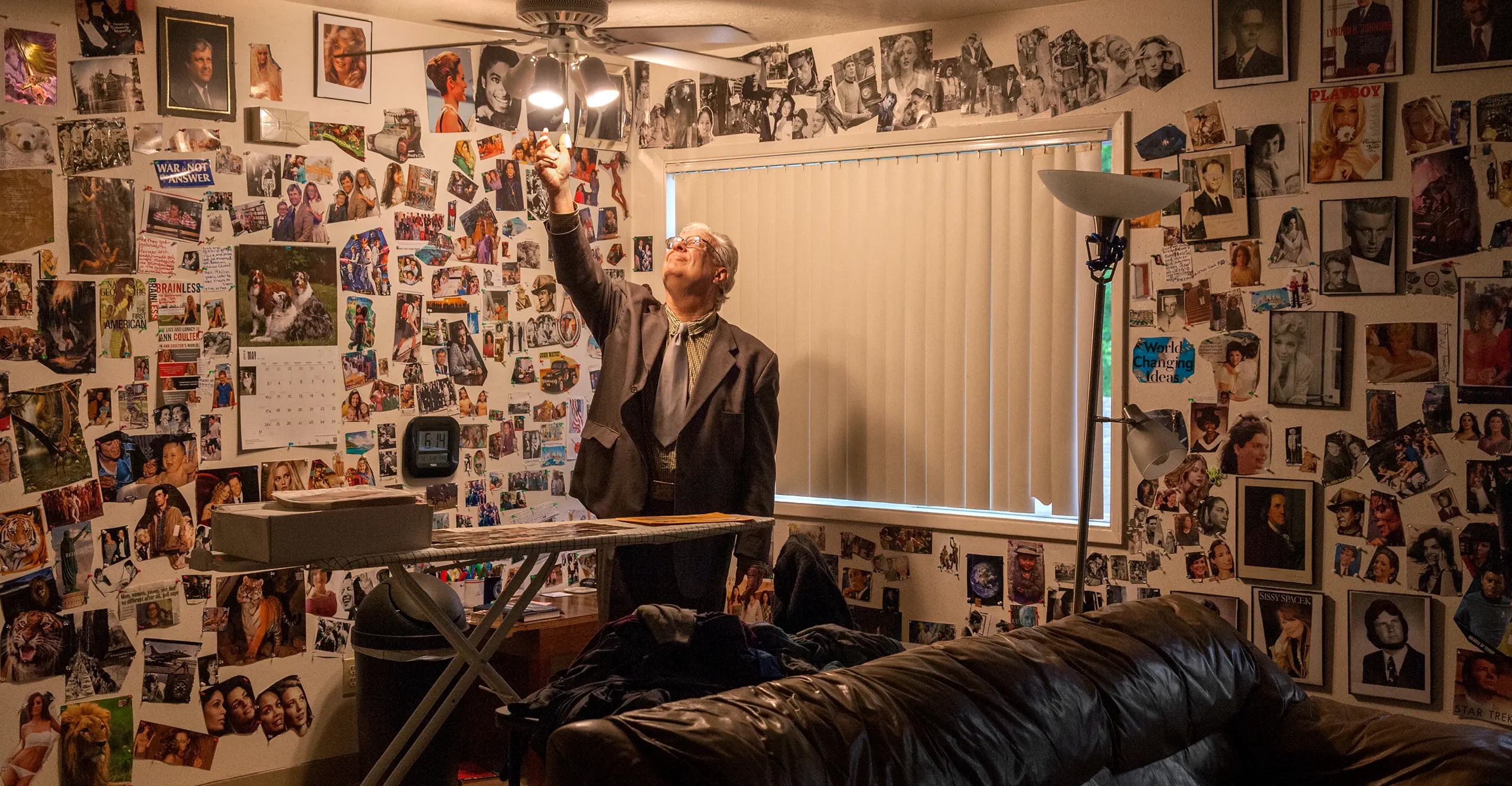 Photograph of an individual standing in the middle of a room with the walls covered in images, with his hand stretch to the ceiling