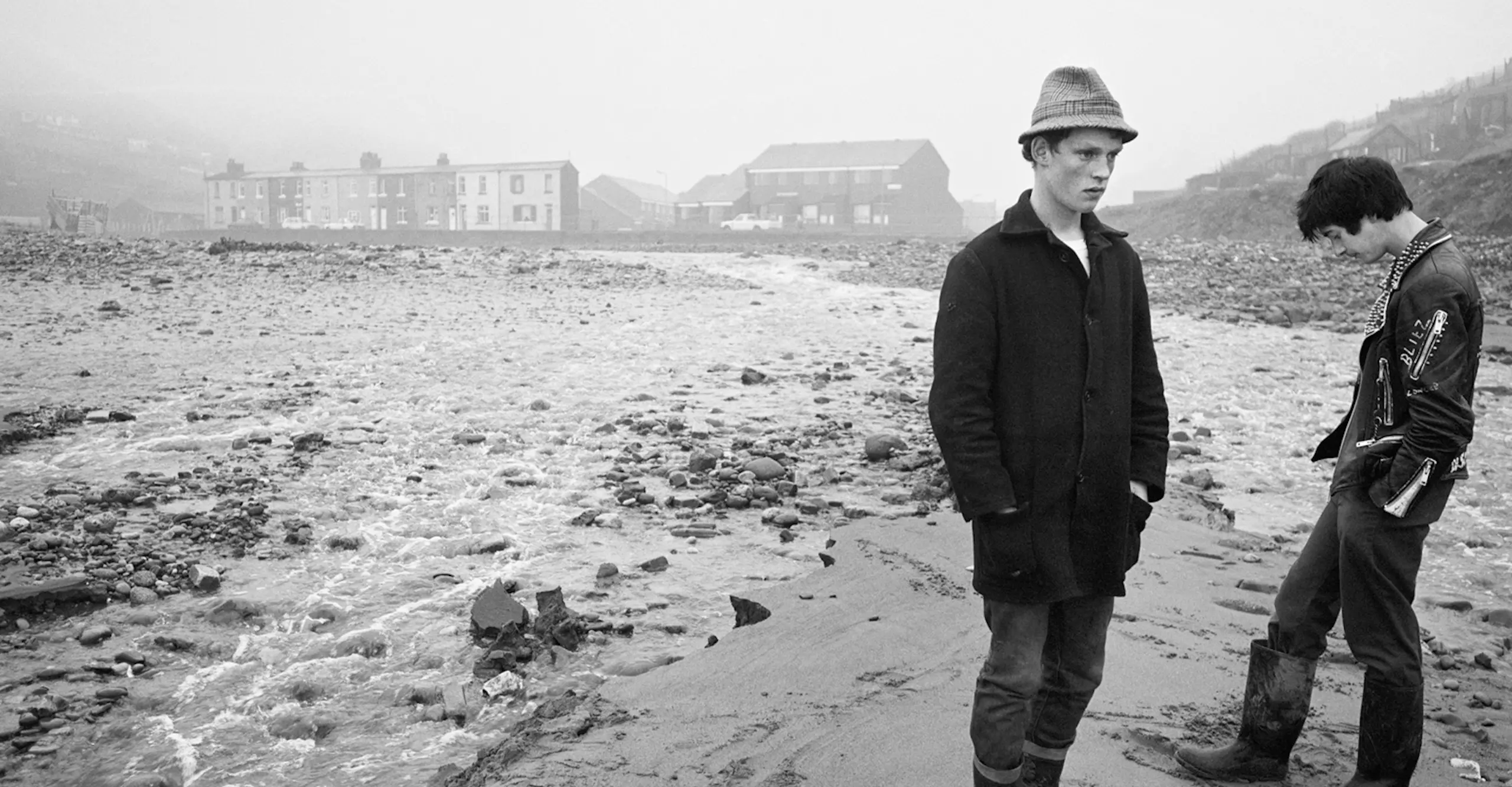Black and white photo featuring two young people standing on a beach on a bleak day.
