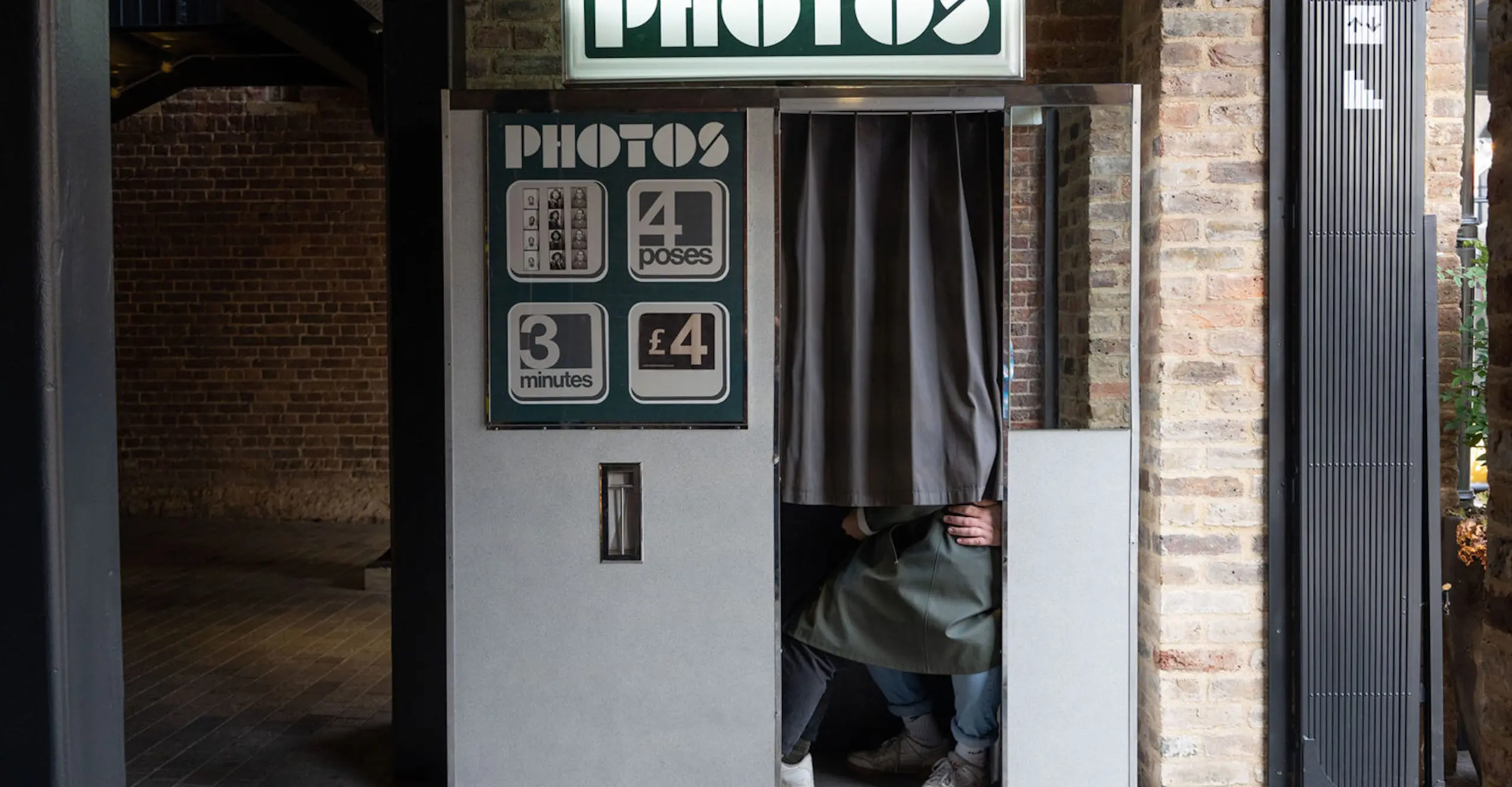 The knees and feet of two people sit behind the curtain of an outdoor photobooth.