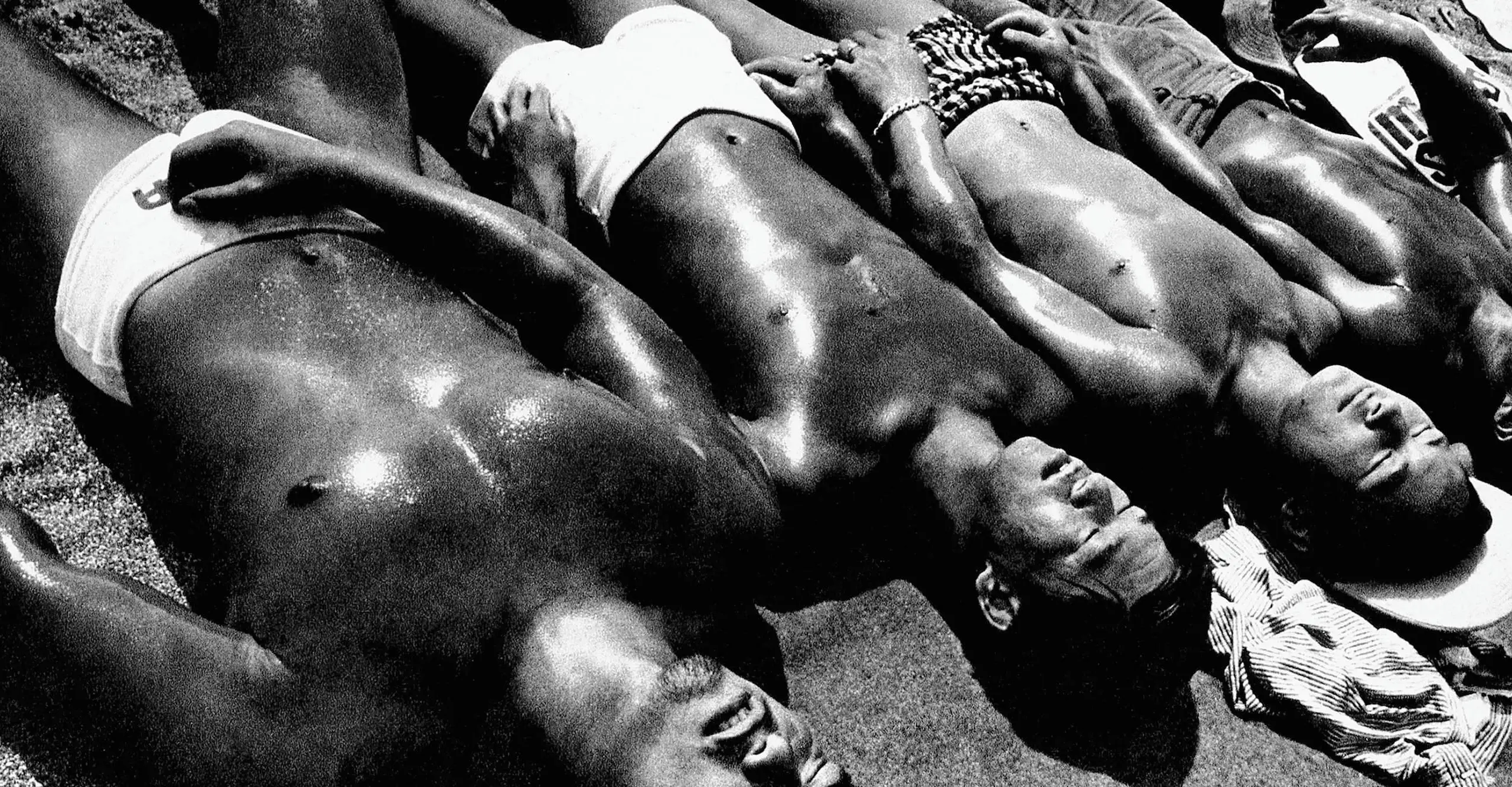 Black and white photograph of a row of shirtless sunbathing men