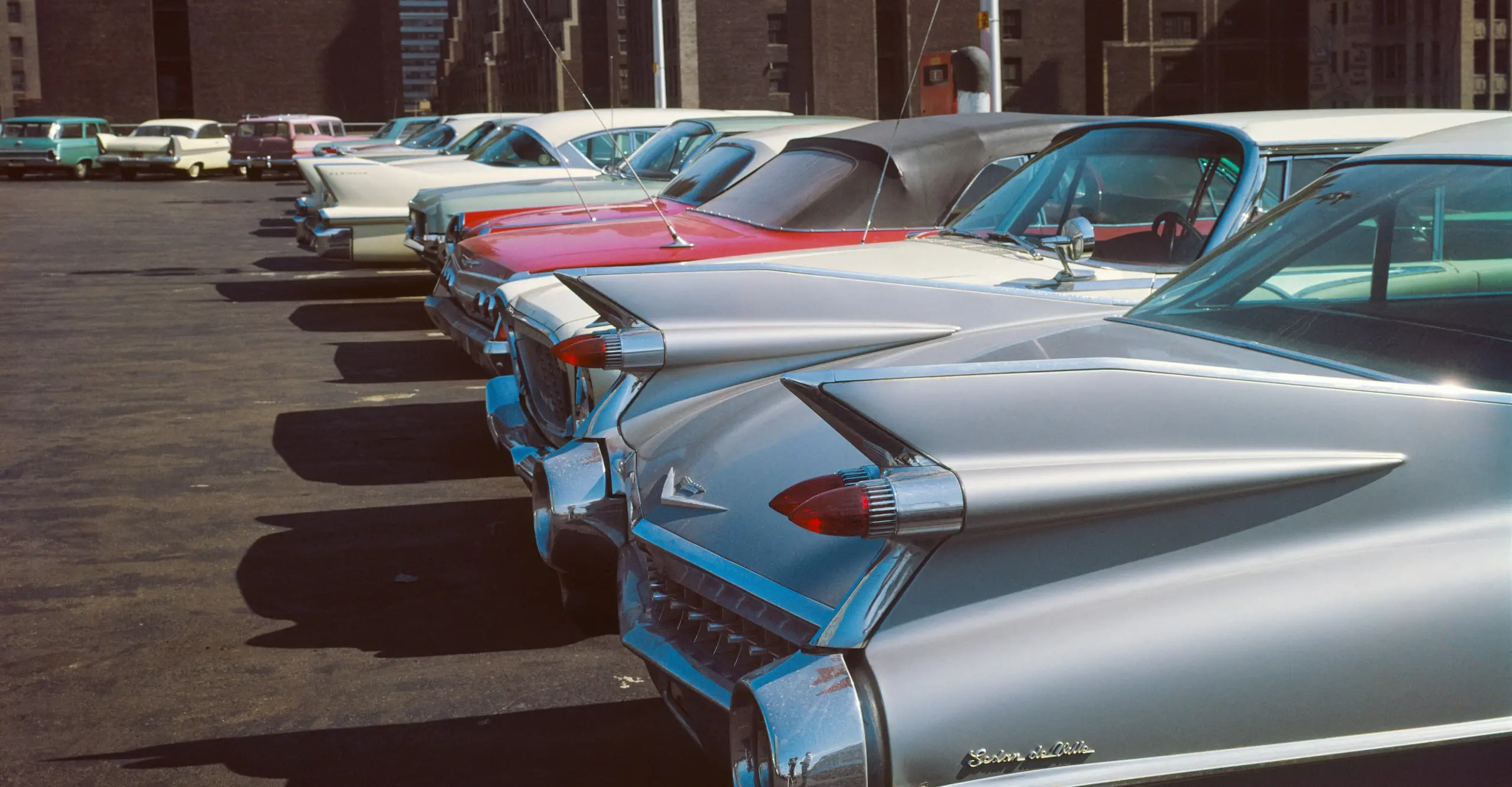 Colour photograph of a row of 1960s cars in a parking lot.