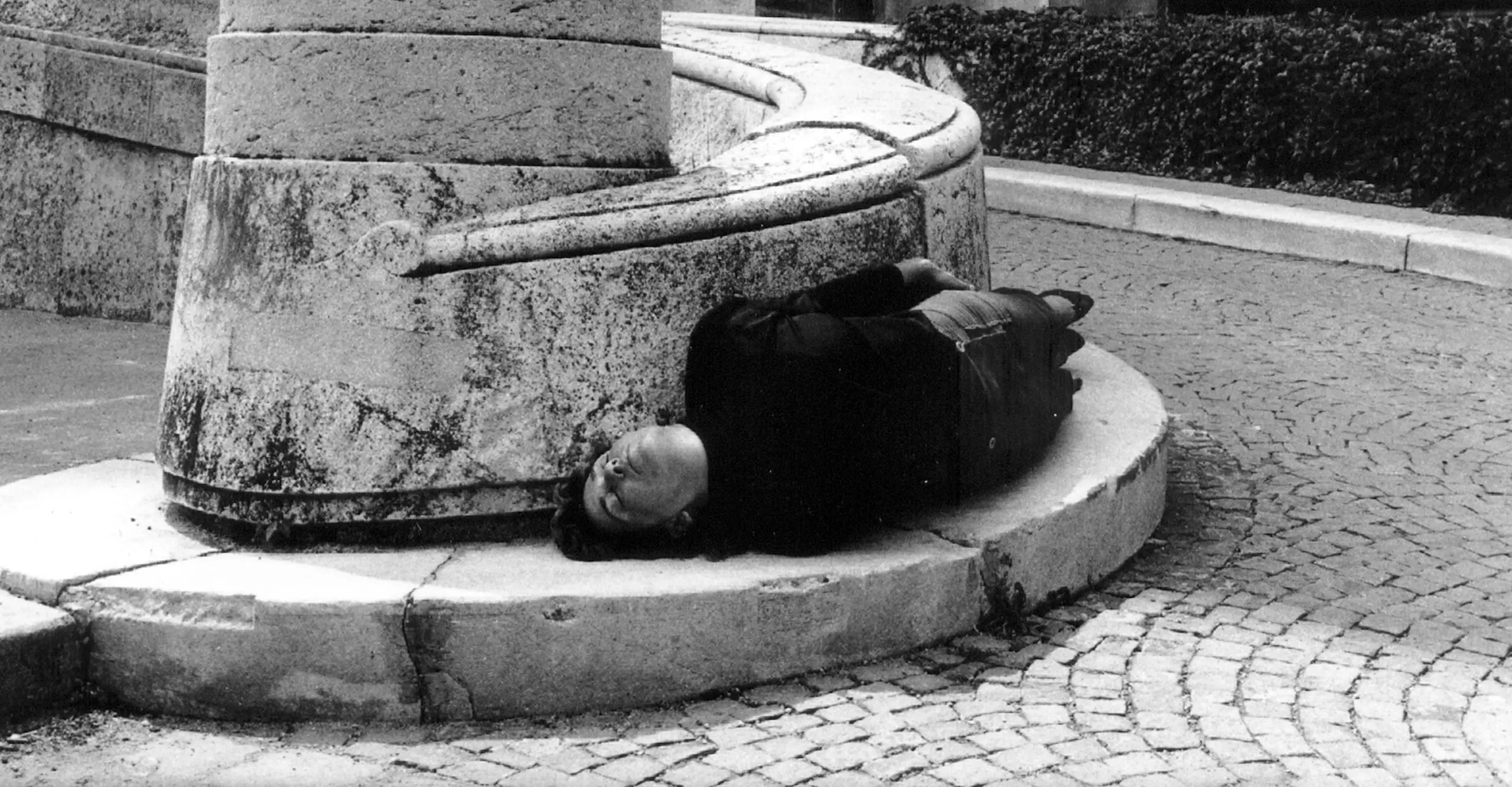 Black and white photo of a person curving their body around a paved wall