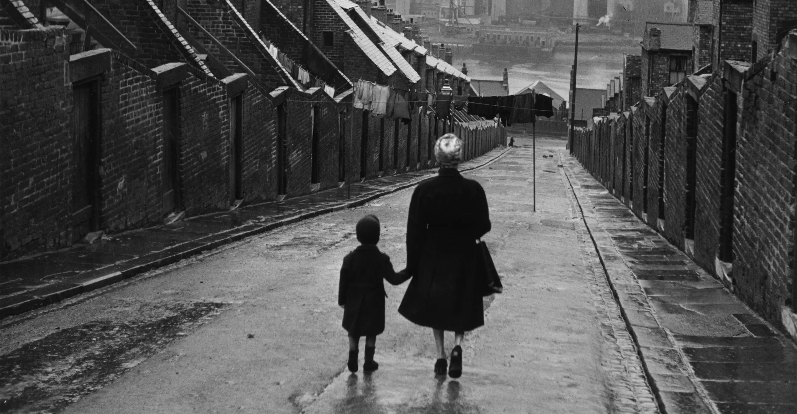 Black and white photo of a woman and child walking down a residential street.