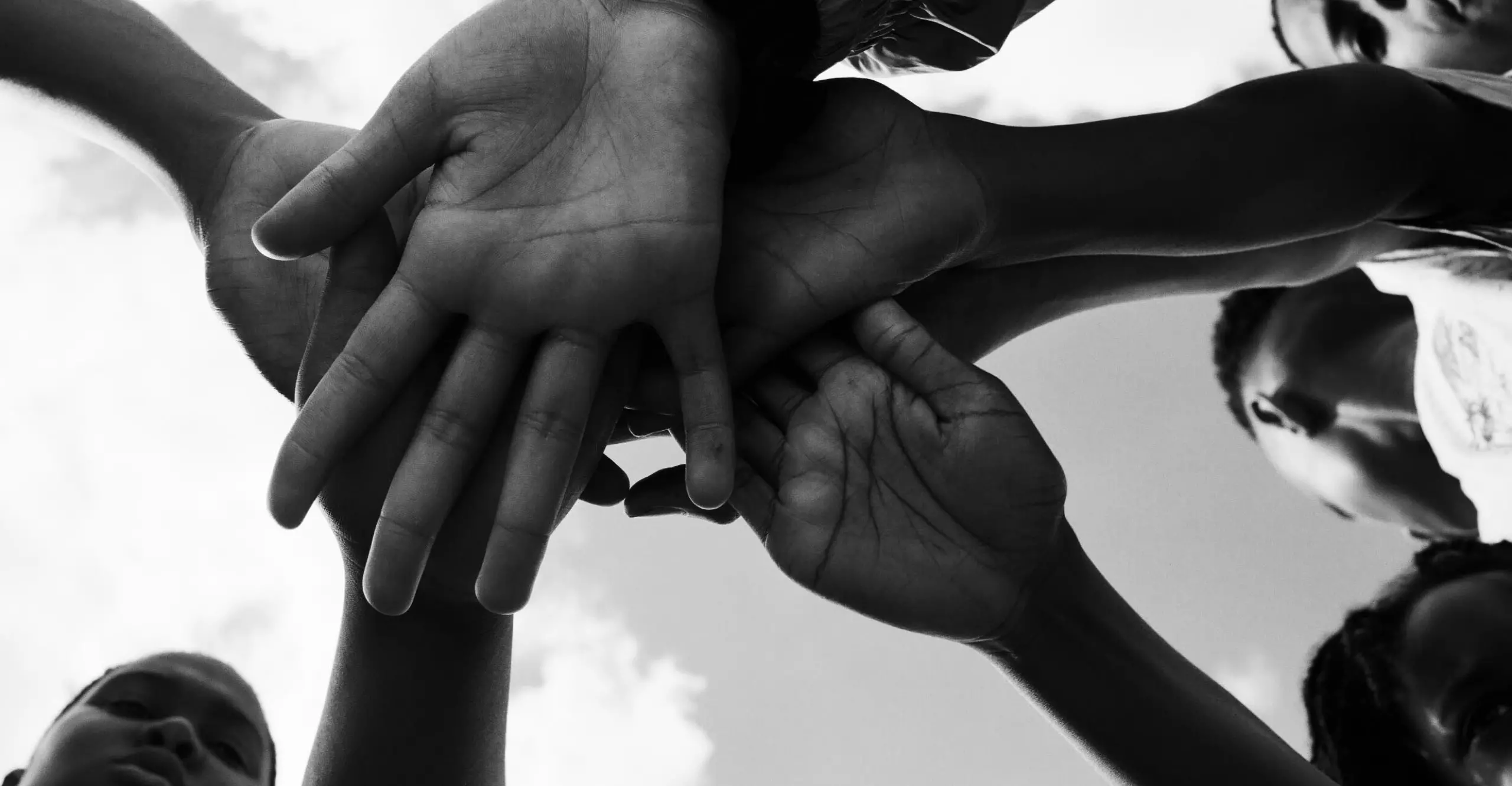 Black and white image taken from below of a group of four children with their hands in the middle, palms facing the camera