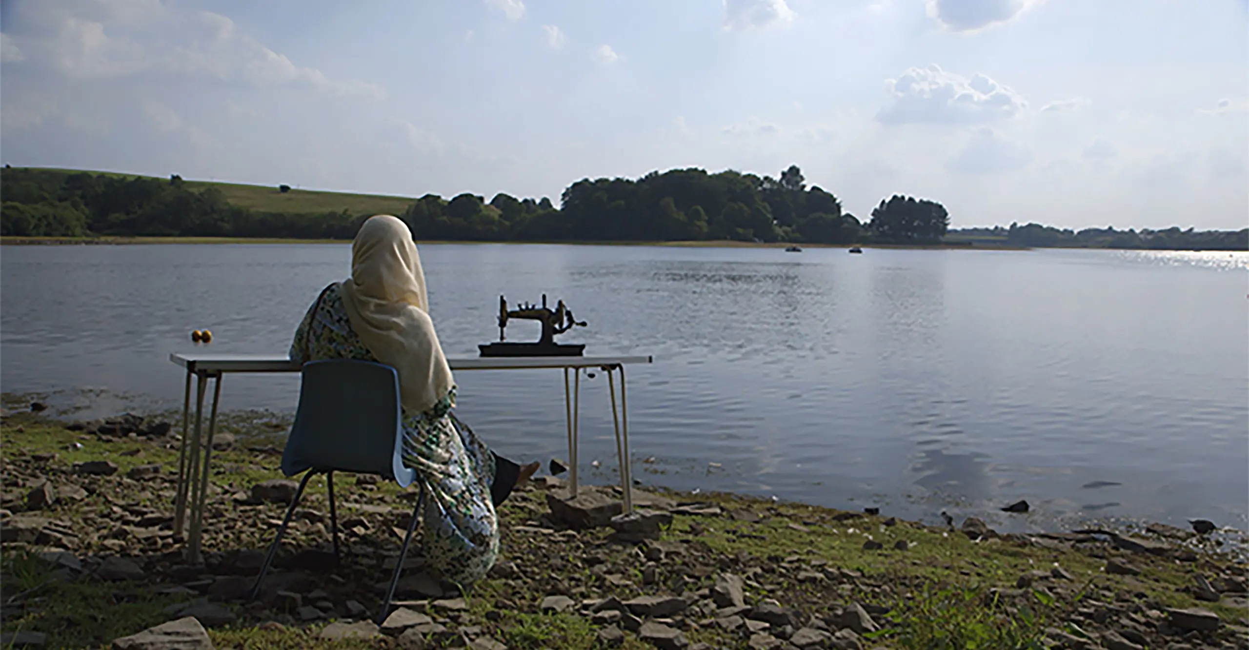 A woman sits overlooking a lake with a sewing machine