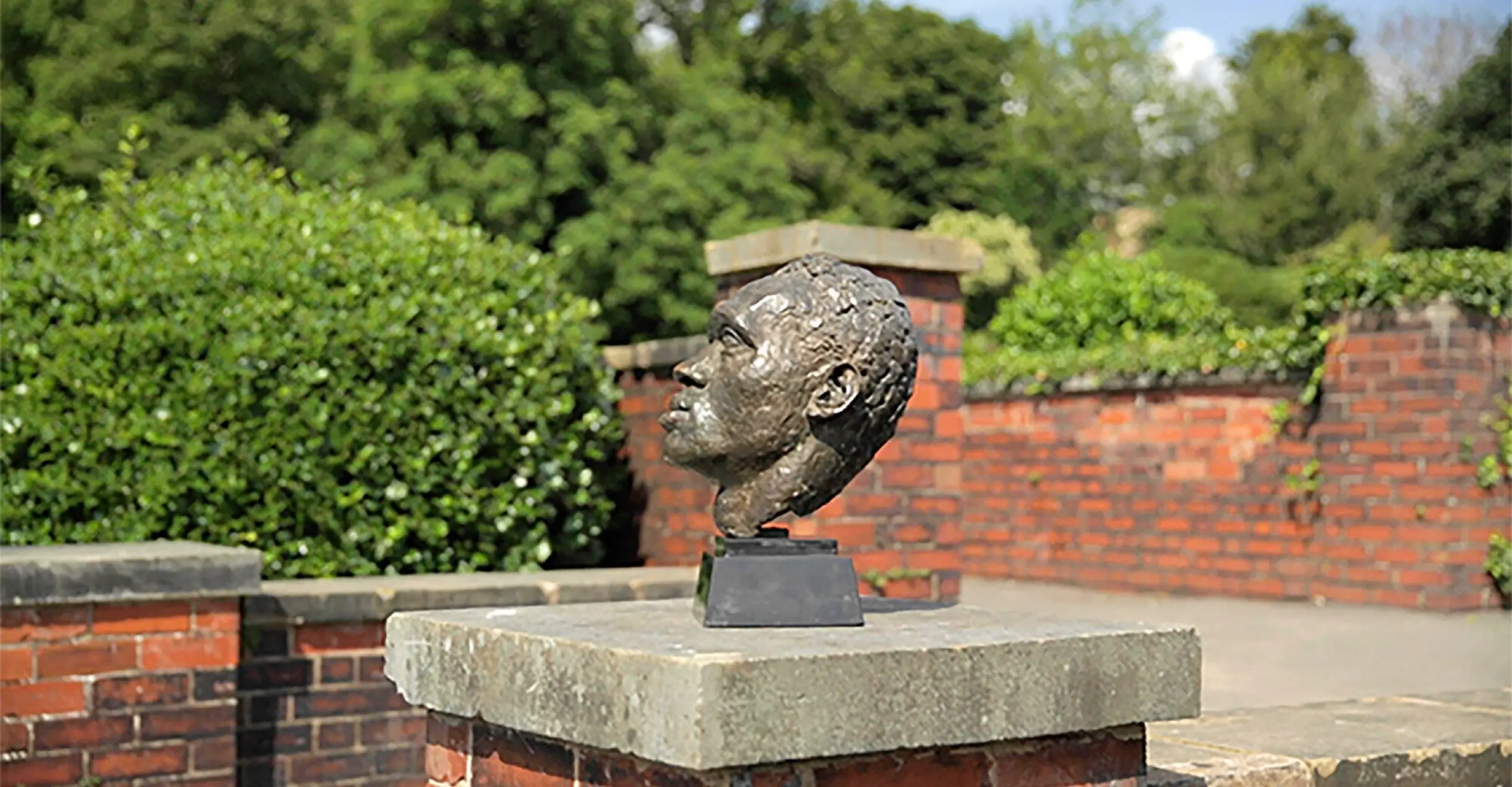 Colour photograph in landscape format featuring a bust of Paul Robeson on cement block outside