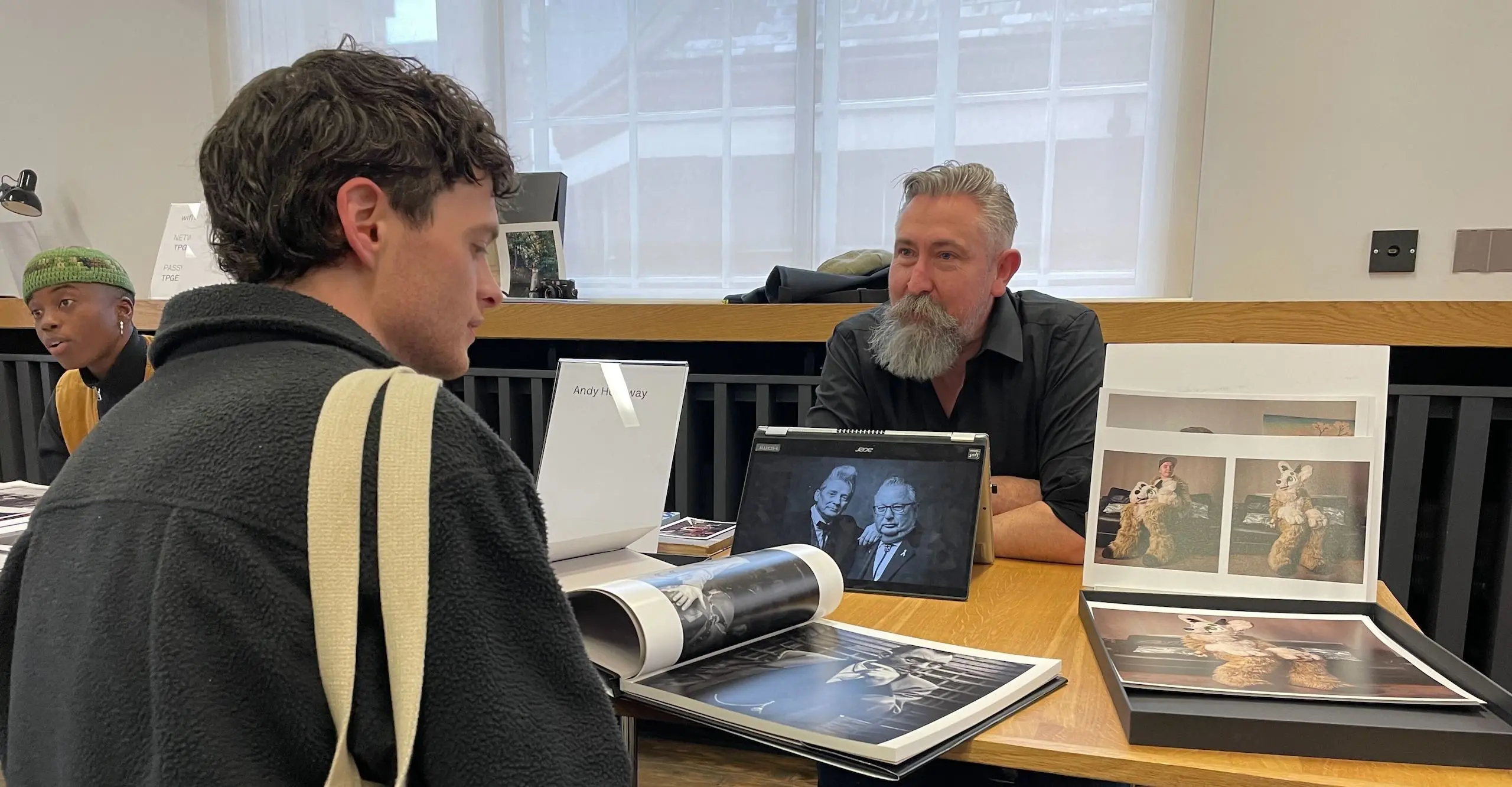Two people sit cross from each other at a table with photo publications in front of them.
