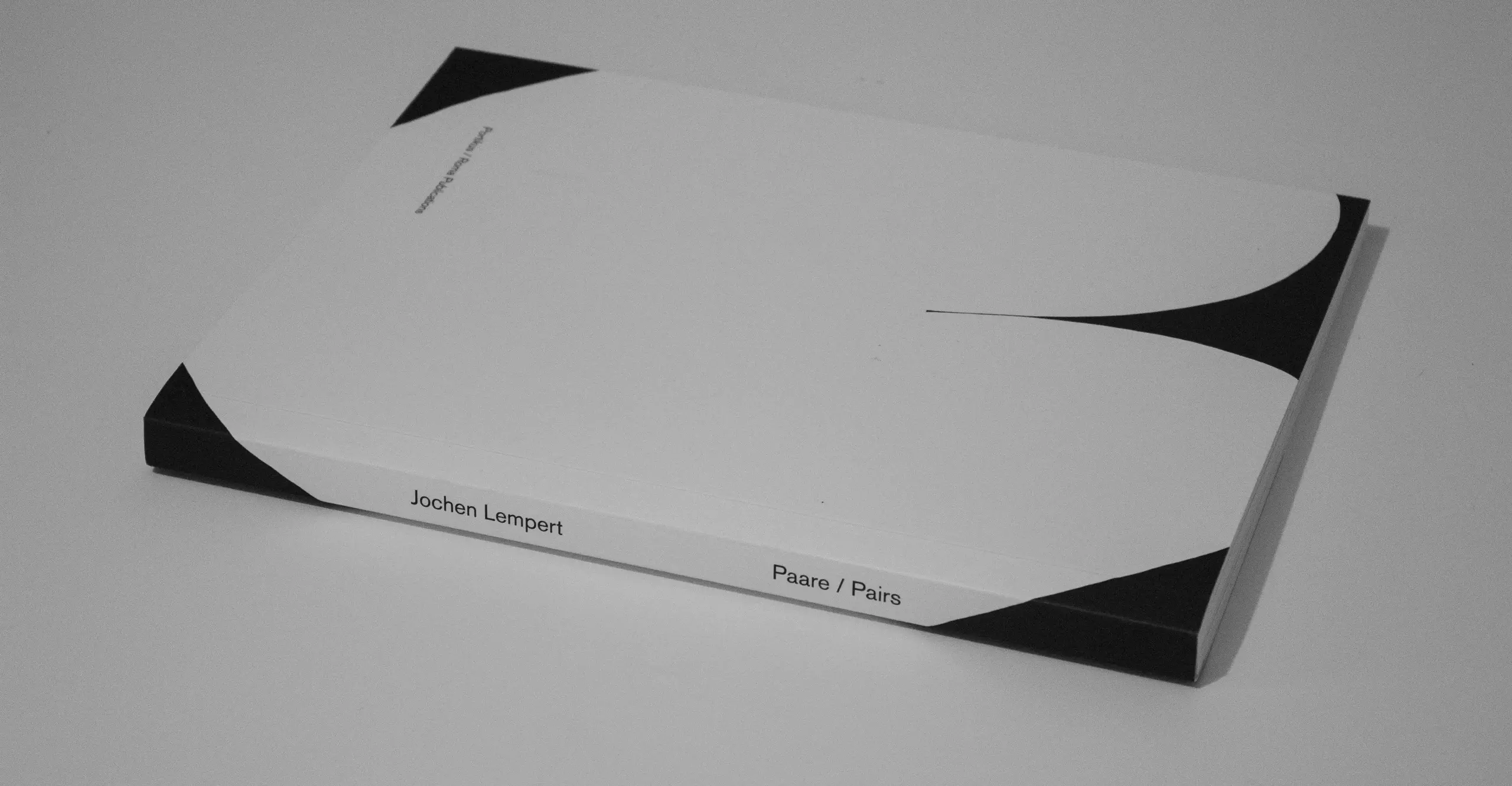 Image of the photobook. It is a short paperback, a white curved shape takes up most of the page with black corners