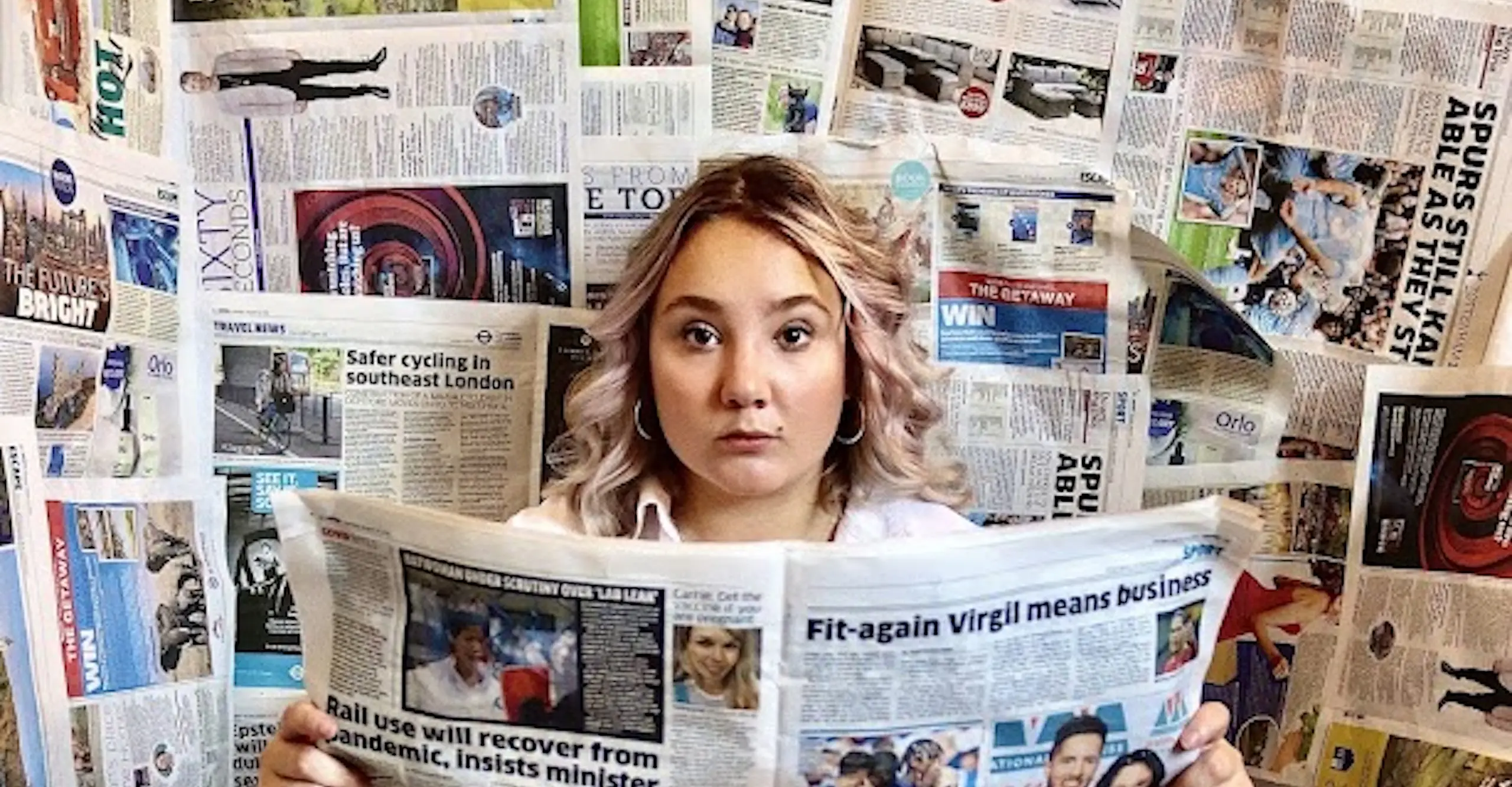A photograph of a person surrounded by newspapers and reading a newspaper. 
