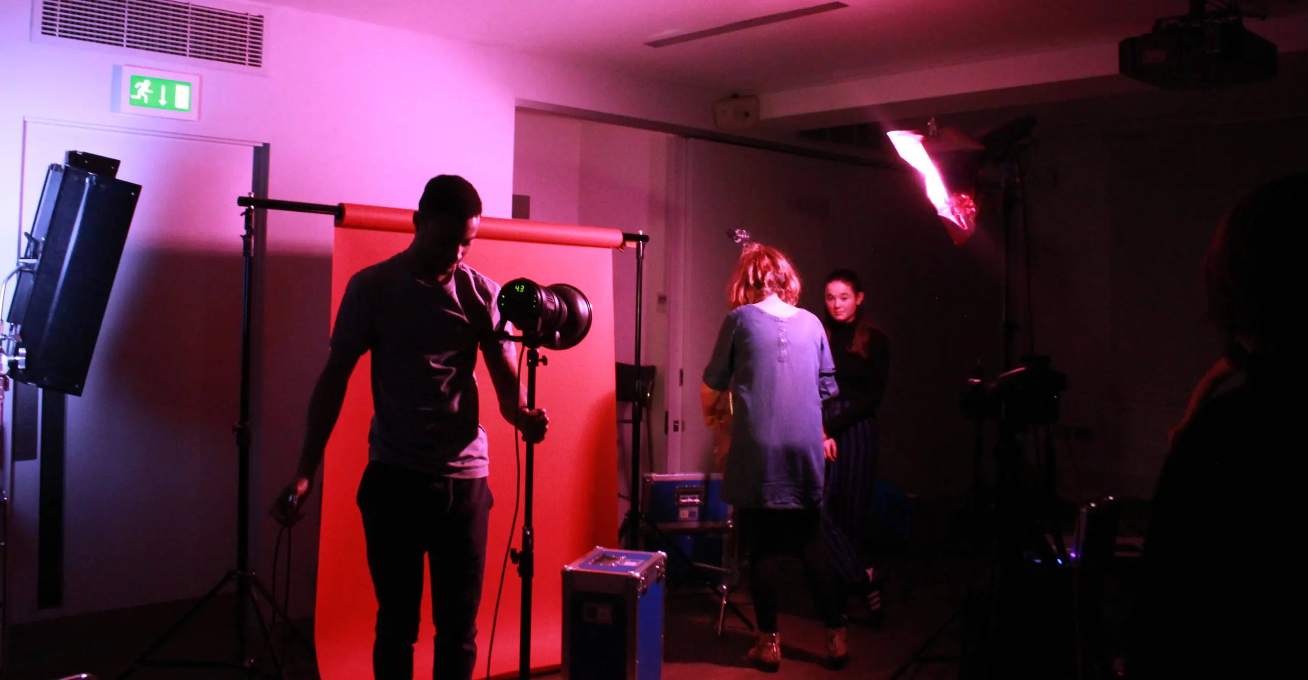 Image of photo studio with pink light, a man in the centre of the room speaks to an audience 