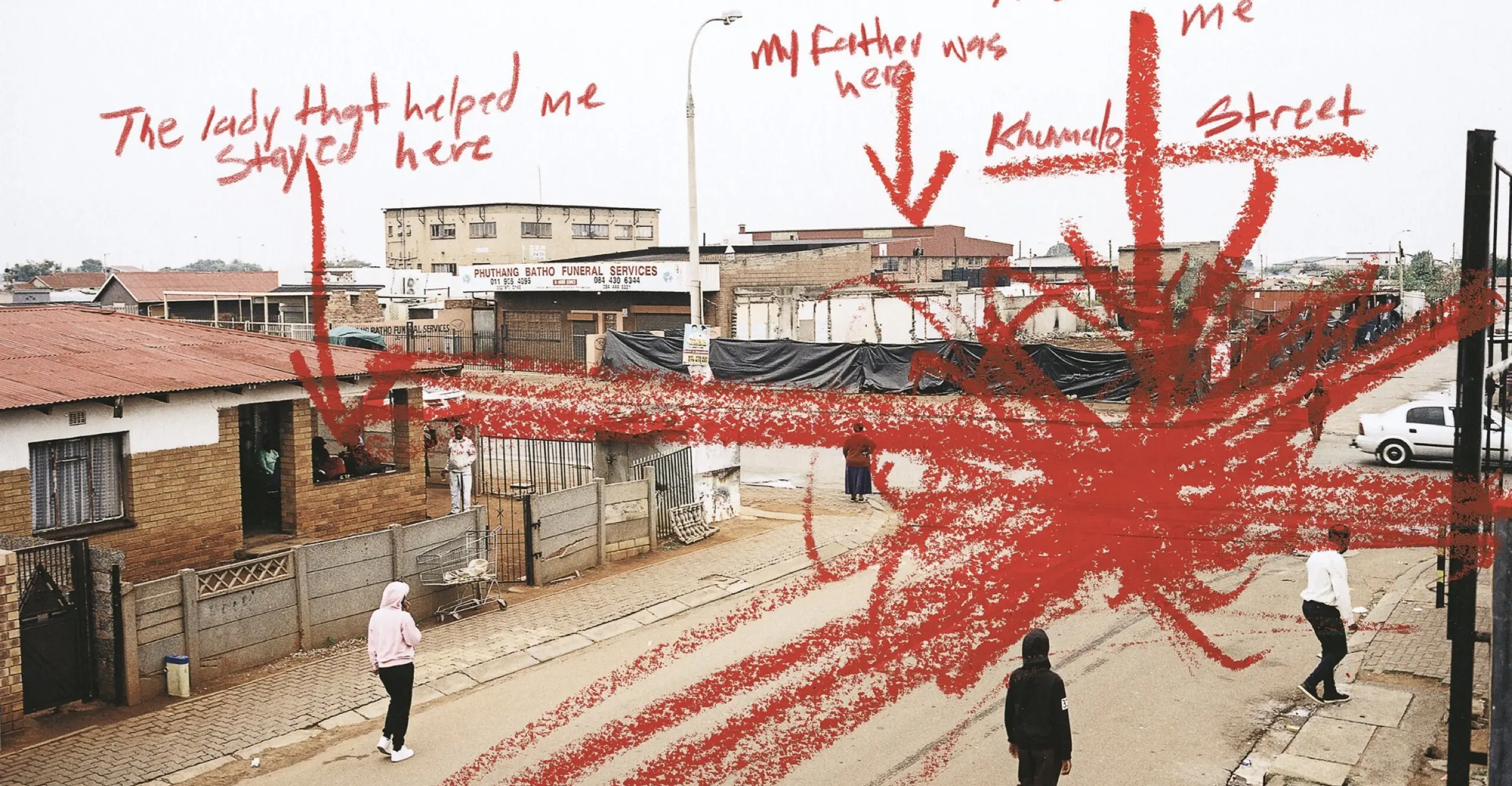 Colour photograph of people stood on a street. The photo is marked with red annotations saying "The lady that helped me stay here", "My father was here", "This is where the car hit me" and "Khumalo Street."