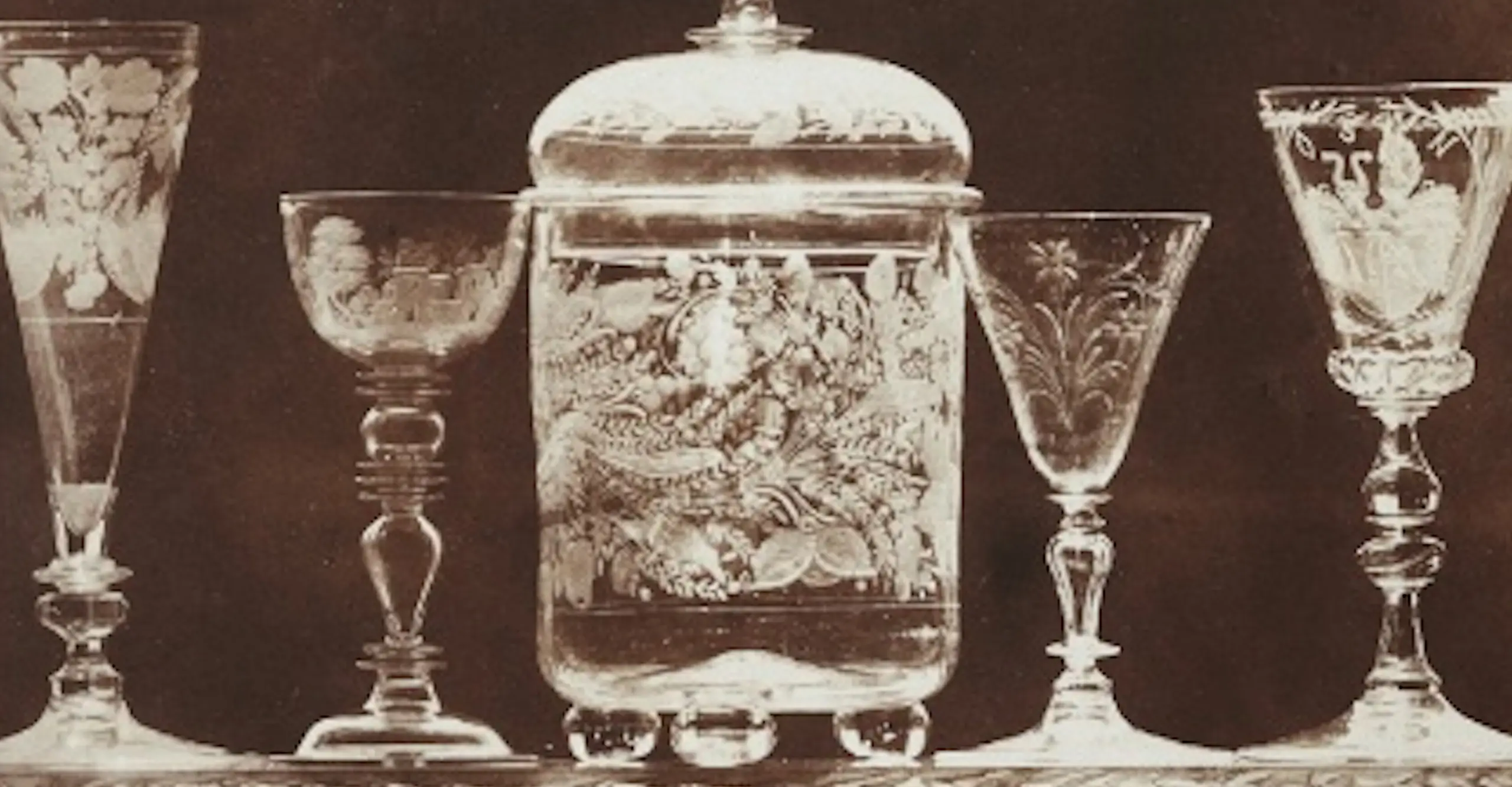 Detail of a brown monochrome photograph of sherry glasses and other glassware lined up on a shelf.