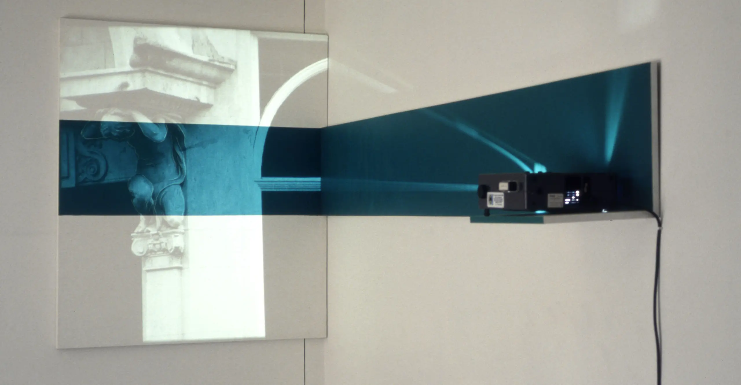A slide projector sends a blue horizontal strip of light onto a black and white photograph of an architectural detail. 