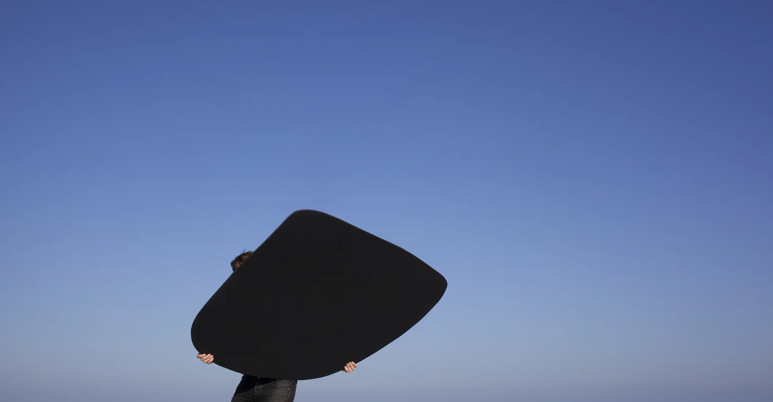 Black triangle held by the artist, silhouetted by a blue sky gradient