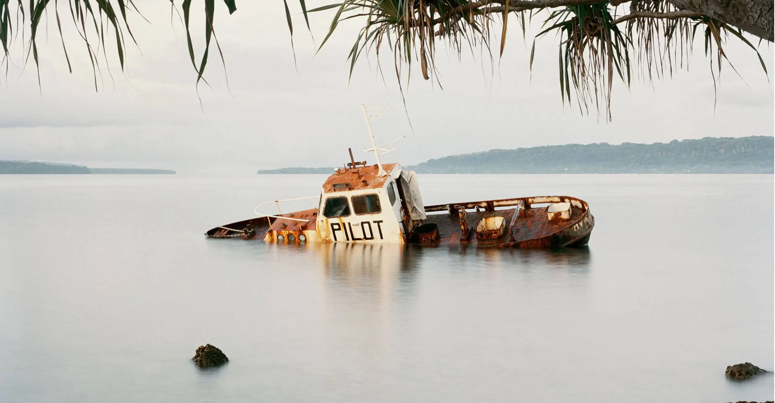 Colour image of partially submerged rusty boat in the water