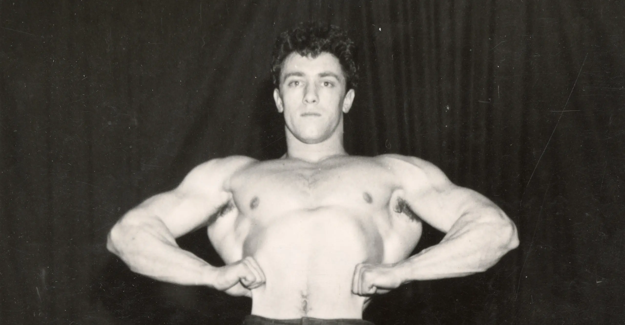 Black and white photo of head and shirtless torso of a man in full muscle pose.