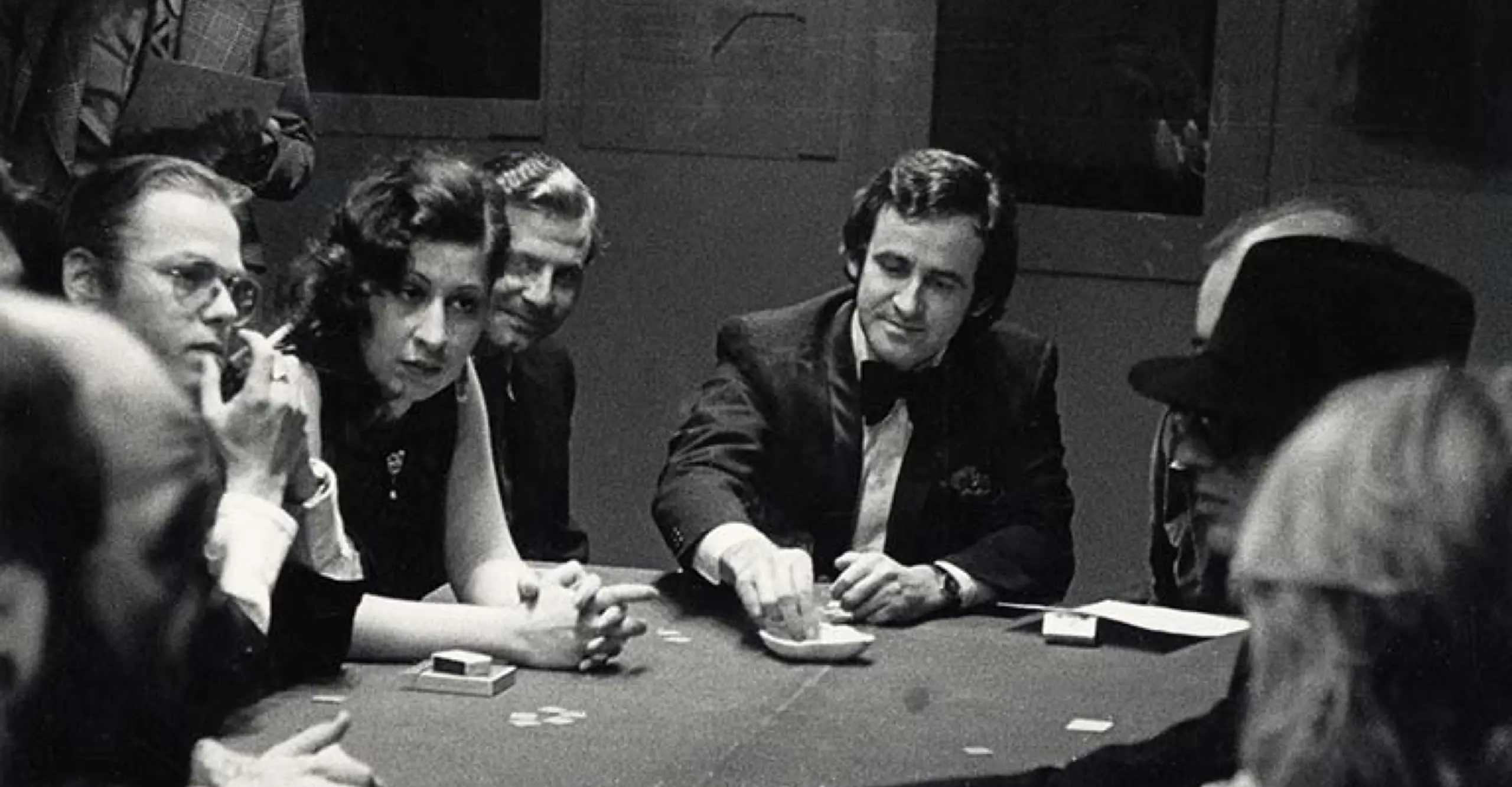 Black and white image featuring eight people seated around a round table playing cards