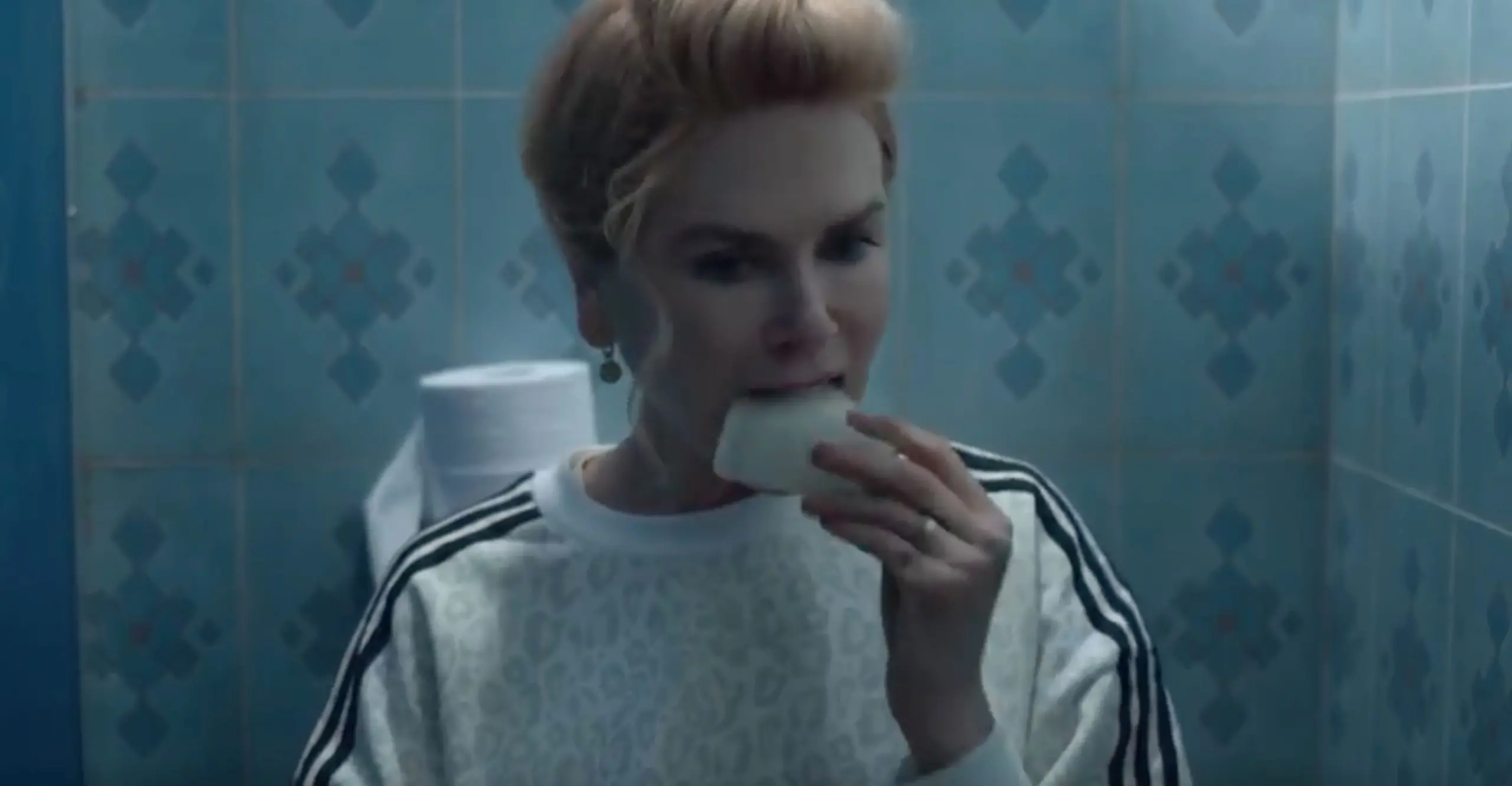 A still image of a tv show in which actress Nicole Kidman is eating a photograph in a bathroom