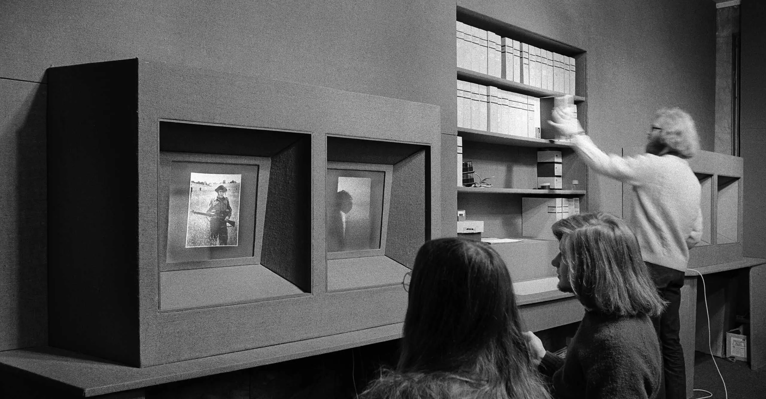 Black and white image of visitors looking at a tv screen