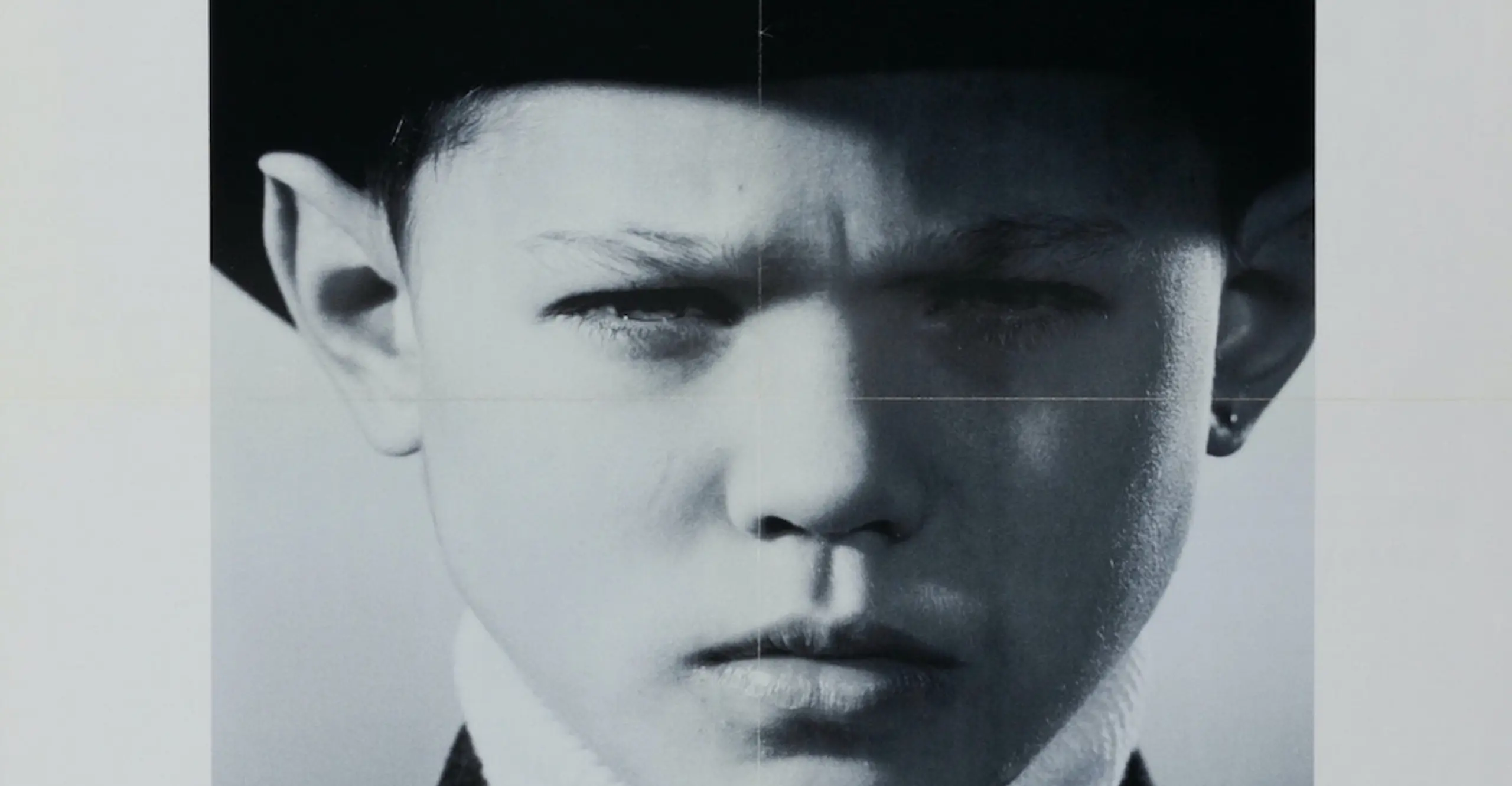 Archival poster featuring a child in black and white wearing a black hat with various typeface above and below the visage