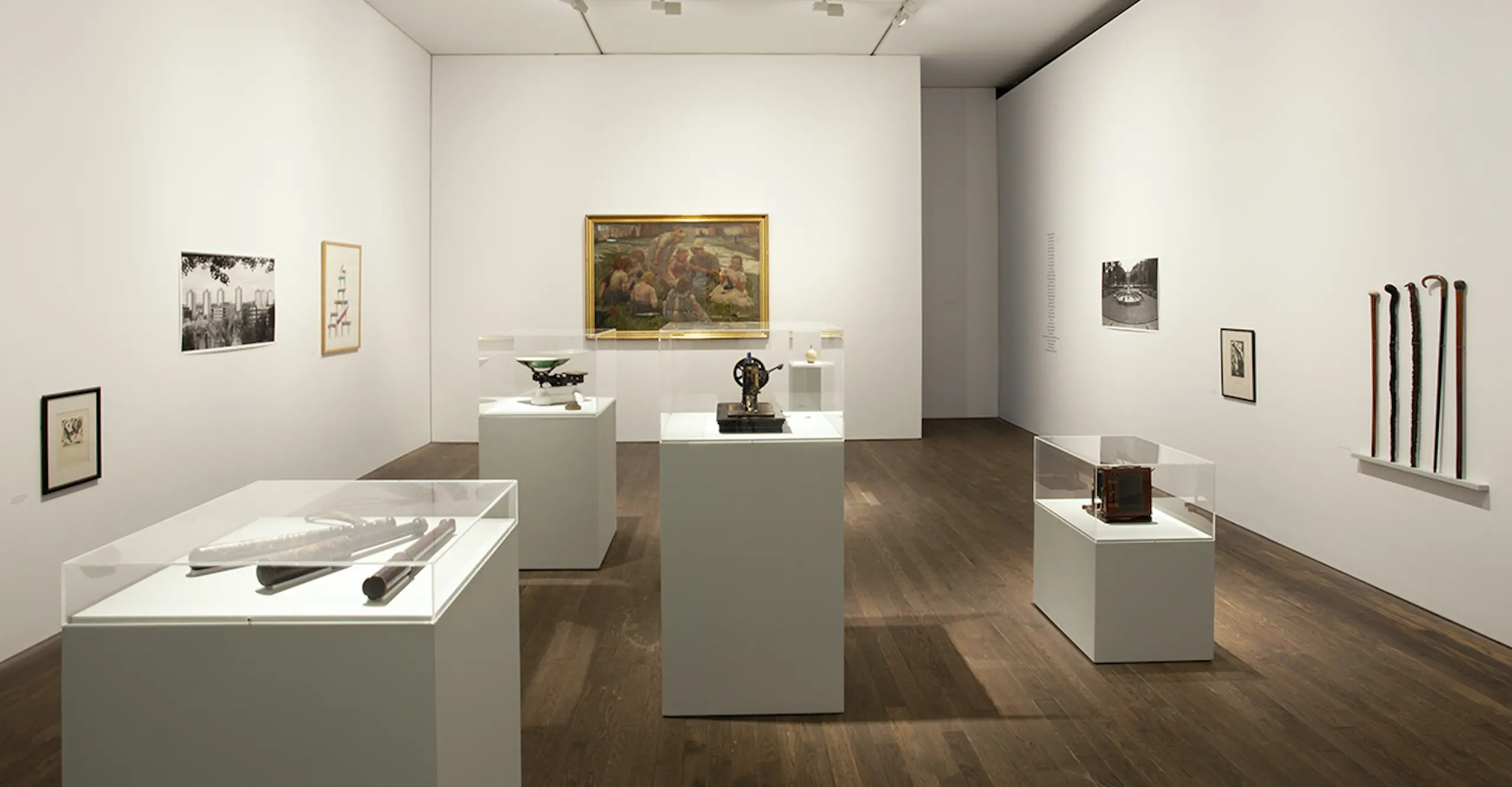 A white gallery room with objects on plinths and pictures on the walls.