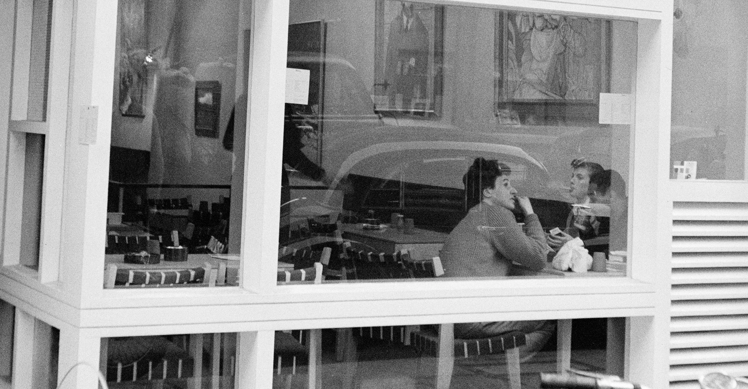Image of The Partisan Coffee House window, showing 2 people inside sitting on a table. Showcased at The Photographers' Gallery in London