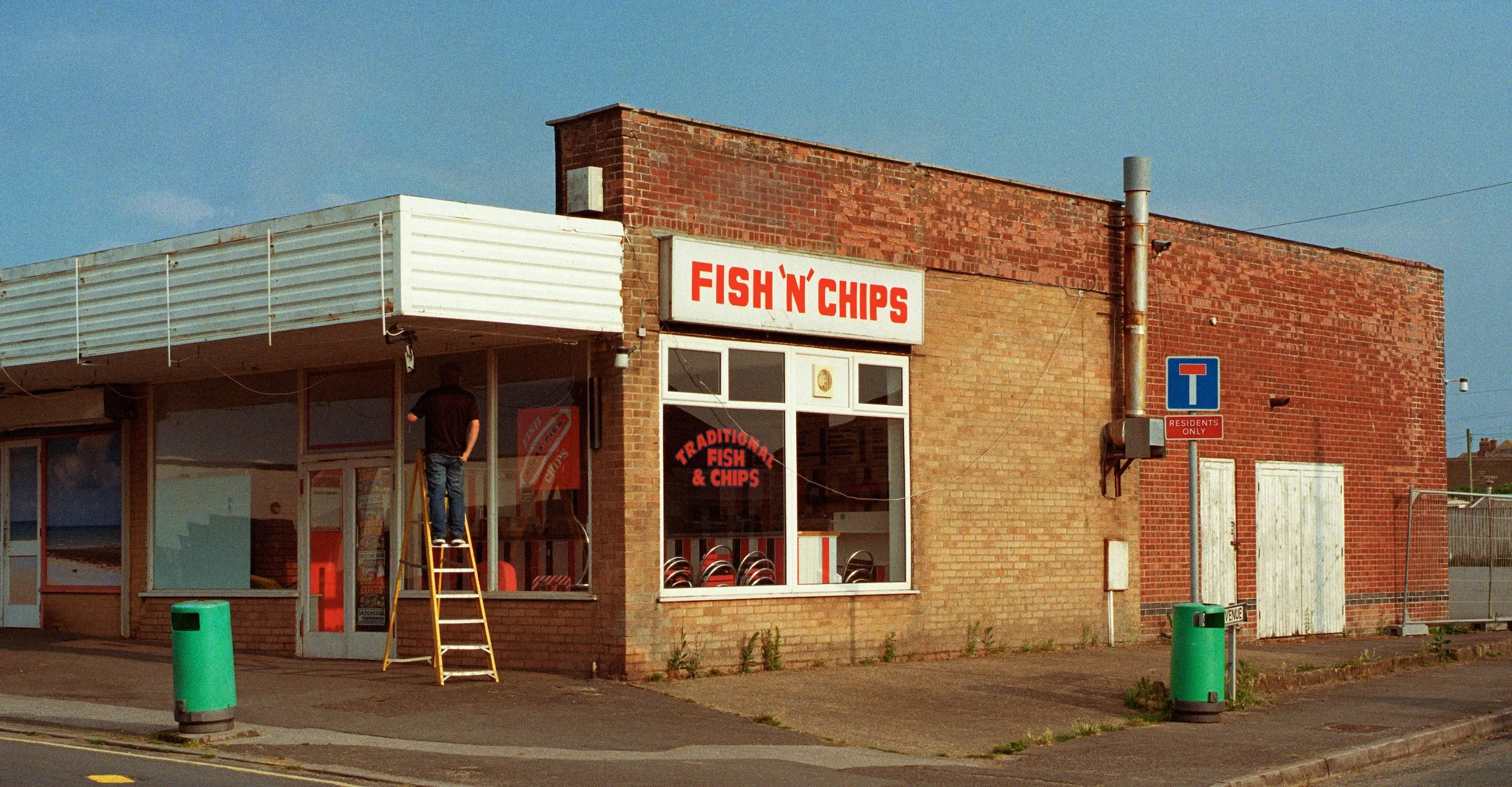 A colour photograph of a street corner fish and chip shop with a bright blue sky behind.