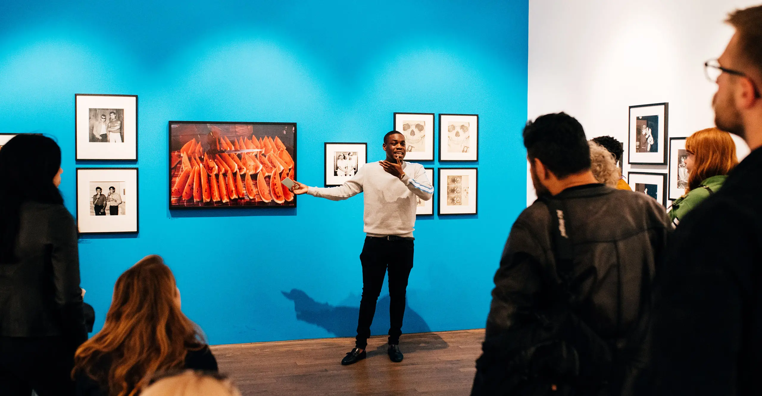 A photograph of a young person speaking to a group of people in a gallery.