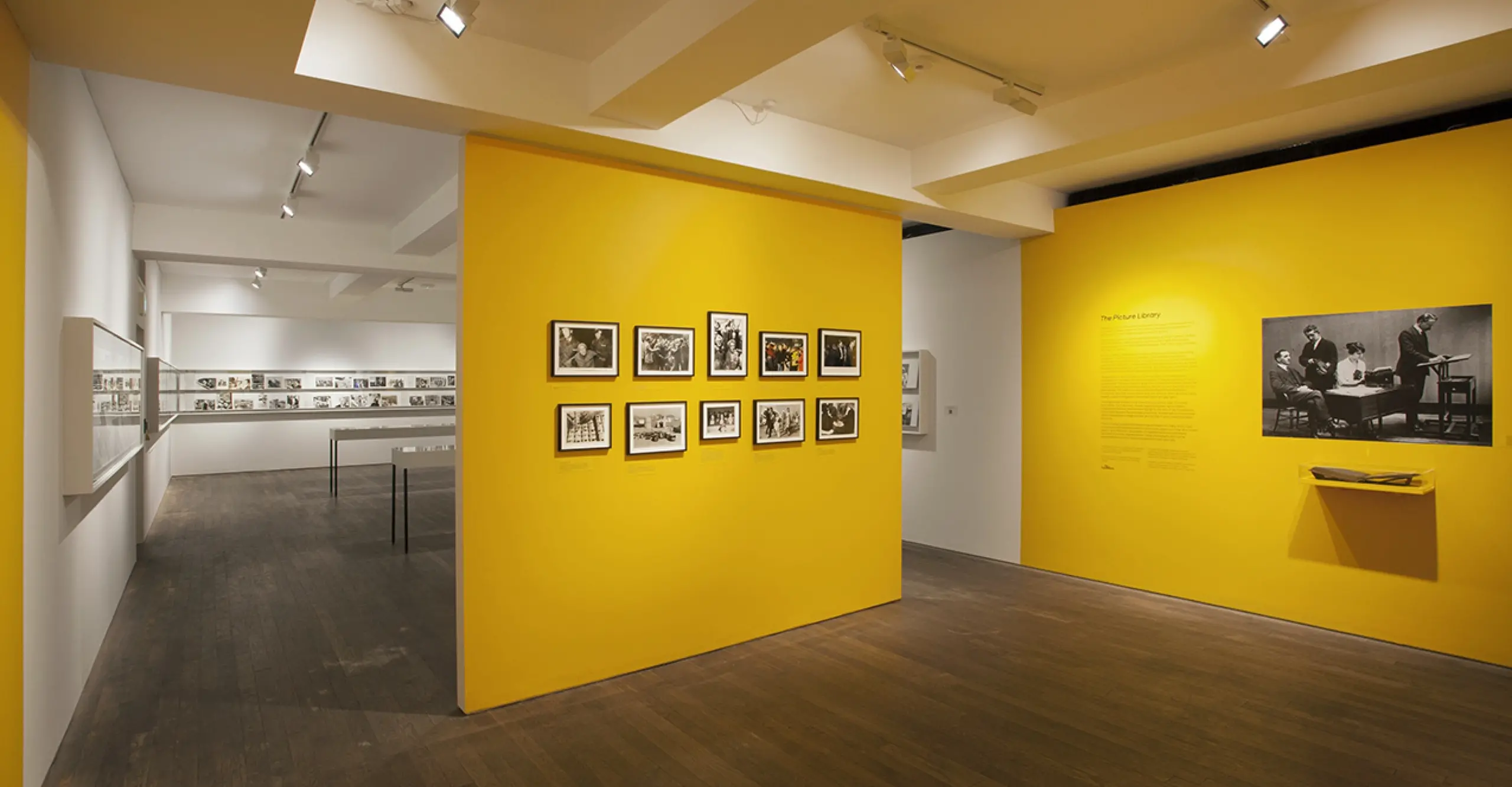 A gallery room with rows of black and white photographs and yellow walls.