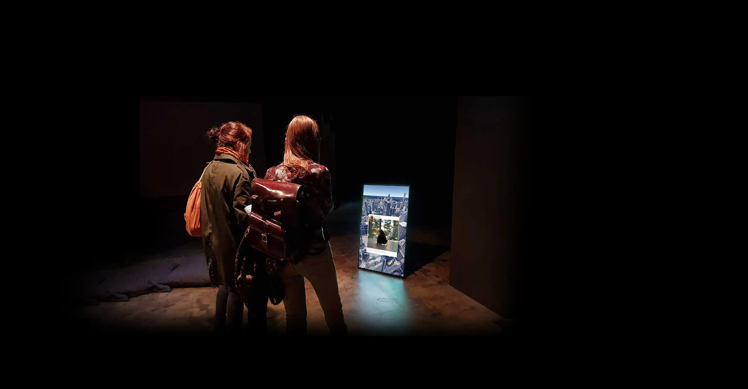 Two people looking at a screen on the floor on a dark exhibition space
