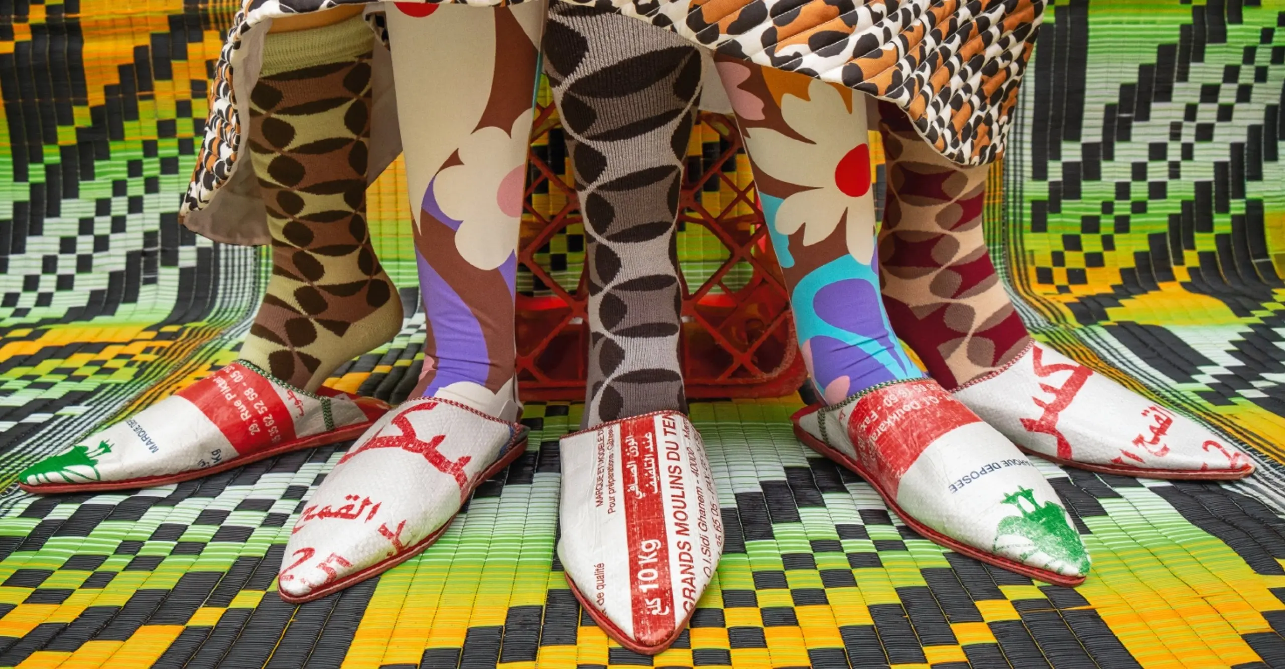 A colourful framed image of three pairs of legs dressed in leopard print, baggy trousers stood on a bright yellow patterned backdrop.
