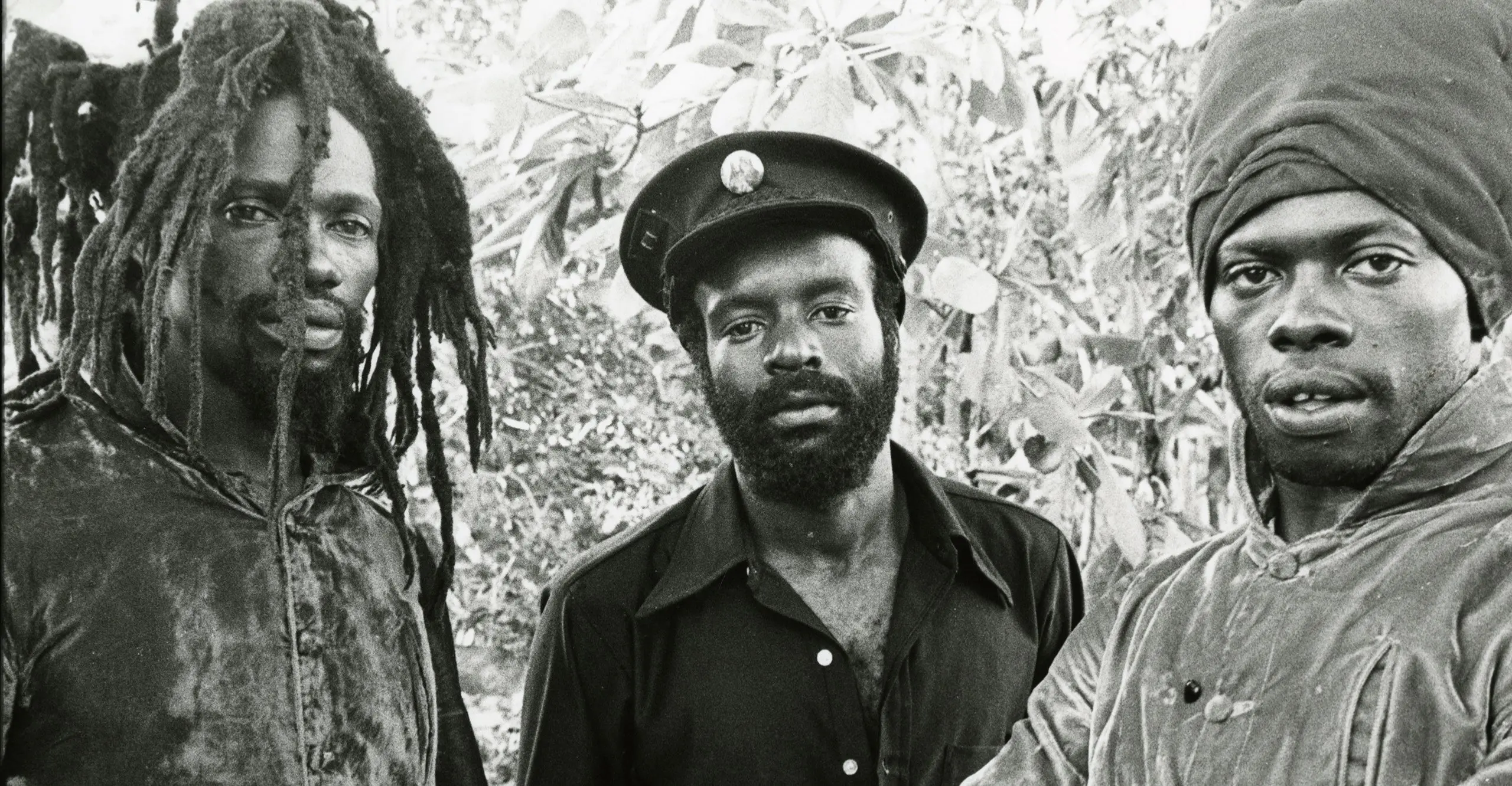 A black and white image of the three members of the reggae group The Abyssinians looking down the camera lens with relaxed expressions.